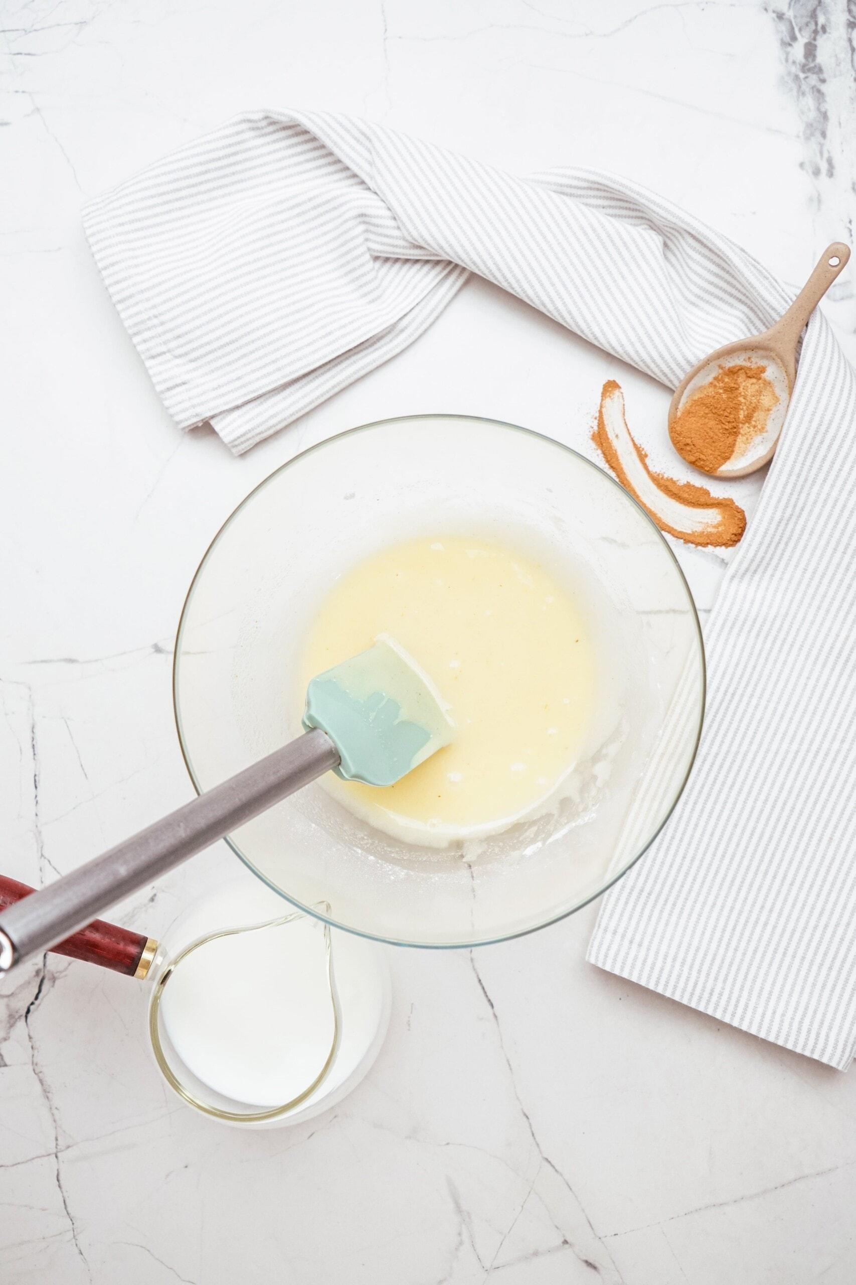 brown butter frosting in glass bowl with rubber spatula