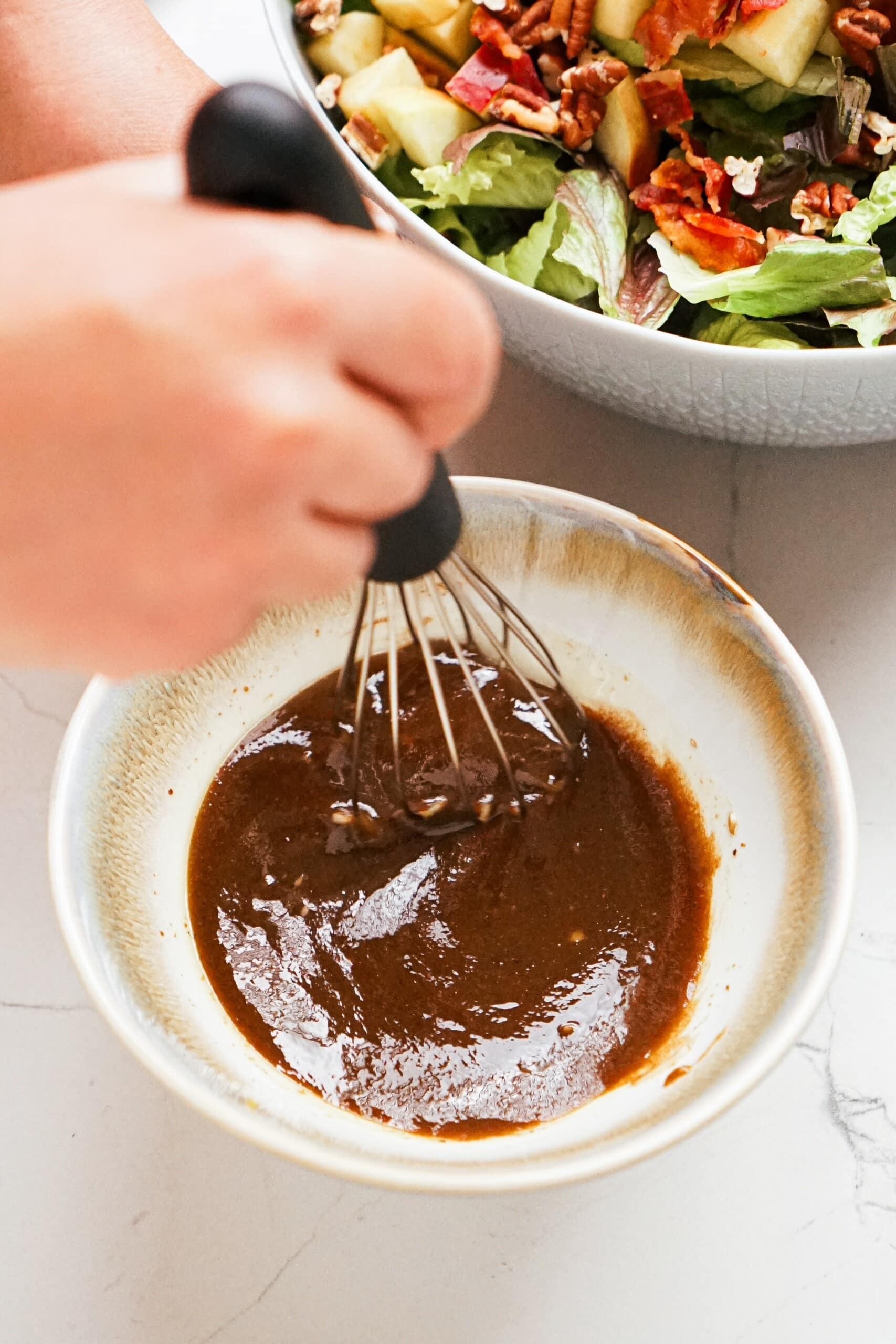 whisking balsamic dressing ingredients together in a bowl 