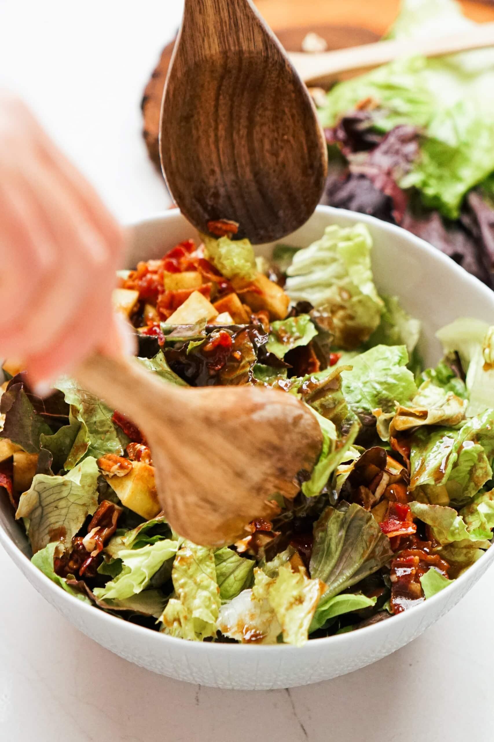 wooden spoons tossing dressing and salad together in a bowl