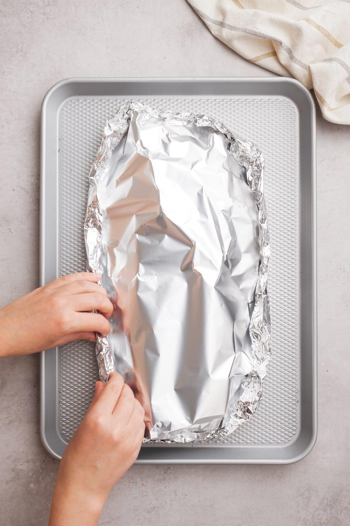 woman's hands wrapping ribs in foil on baking sheet