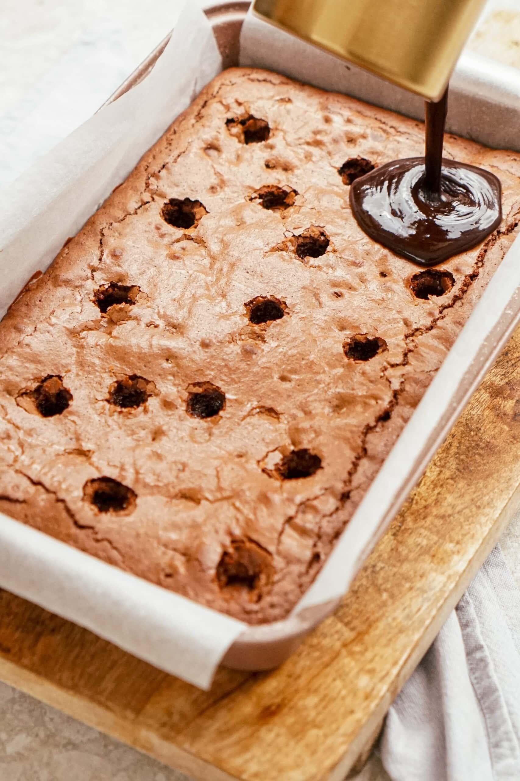 pouring hot fudge sauce over brownies, filling the holes with hot fudge