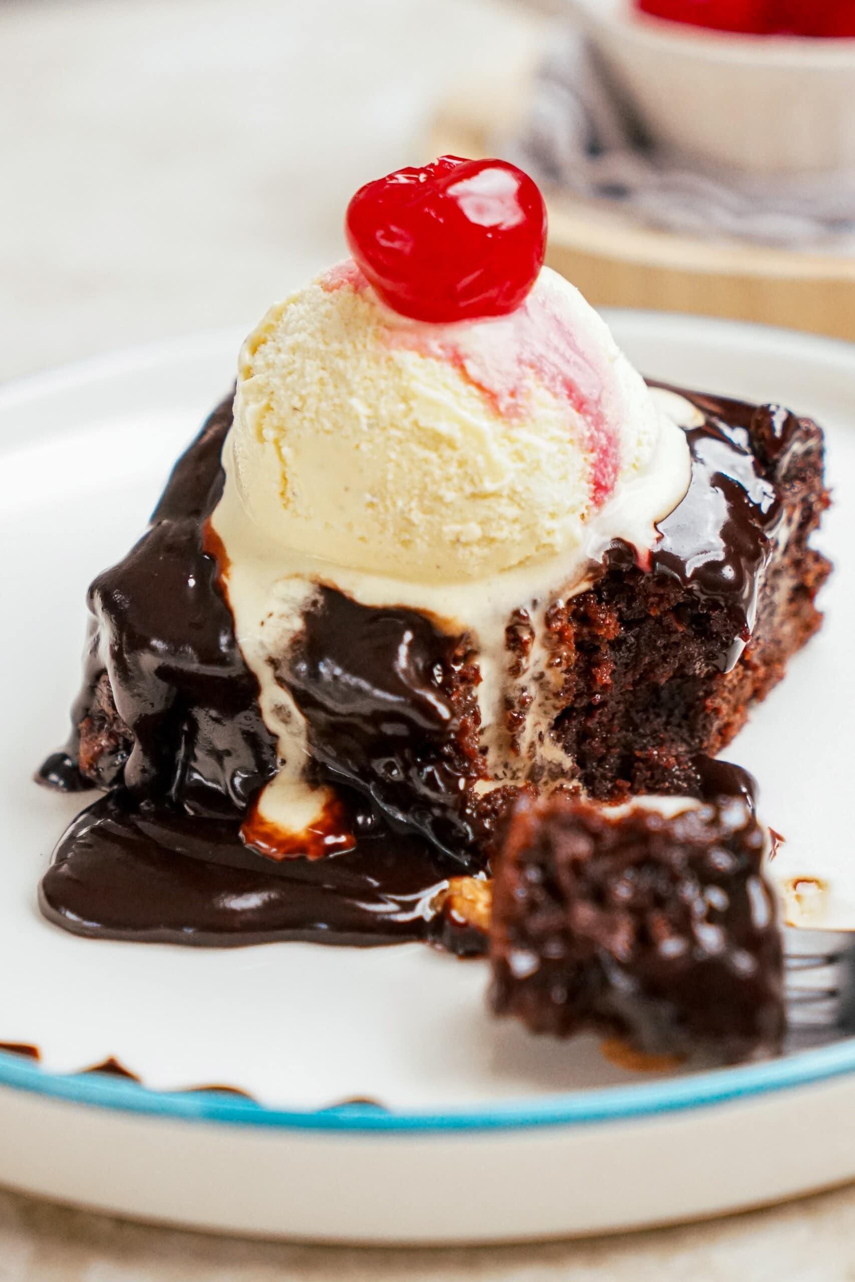 hot fudge brownie square on a plate with vanilla ice cream and a cherry on top