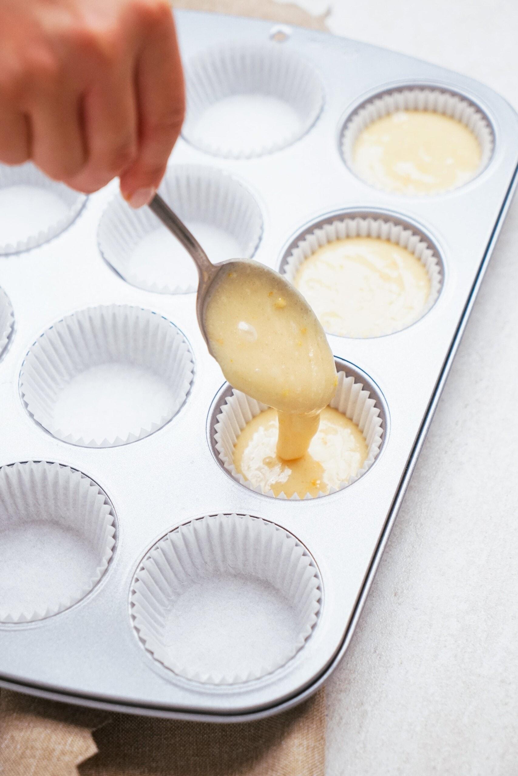womans hand using a spoon to fill cupcake liners