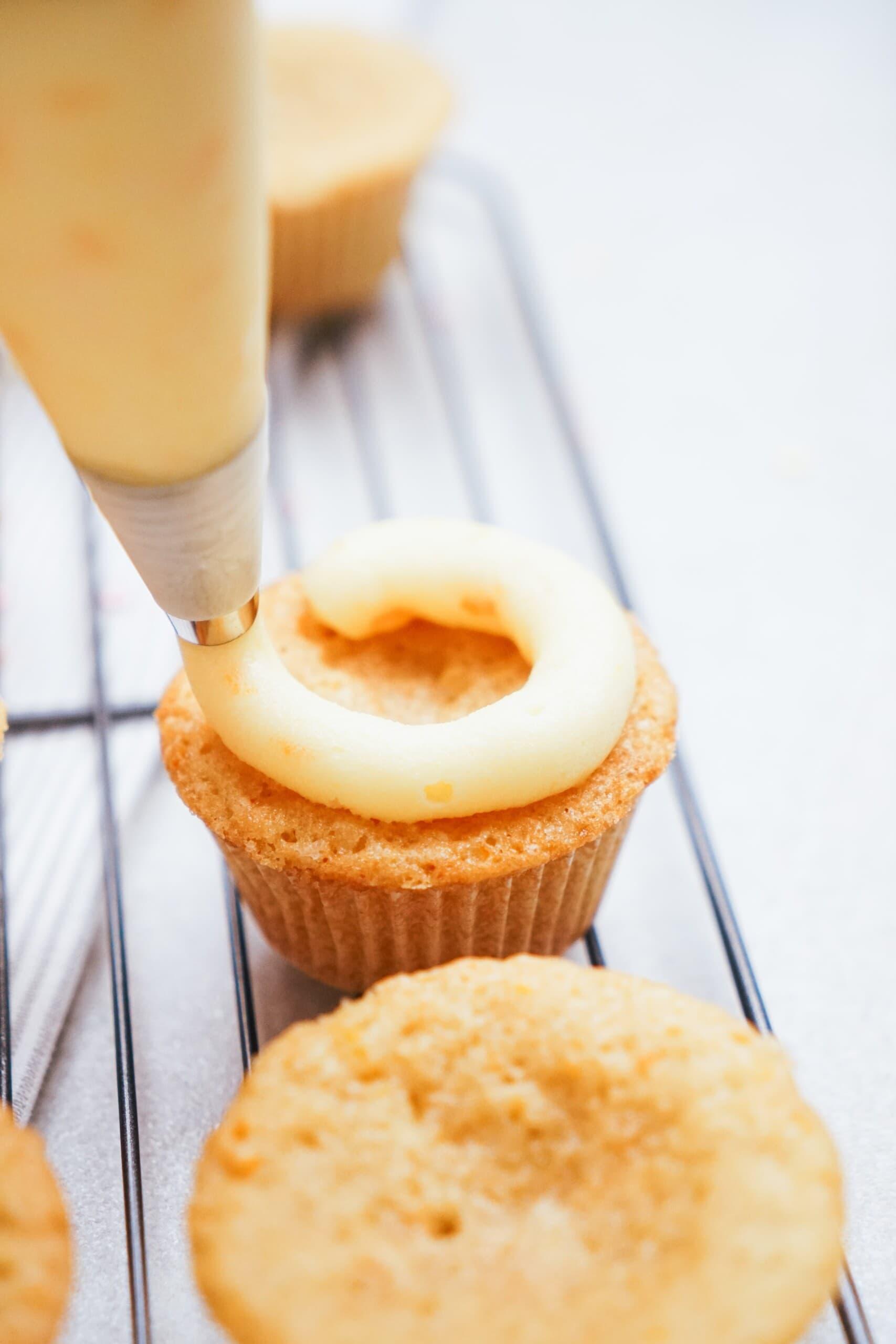 adding frosting to a cupcake with a piping bag and tip