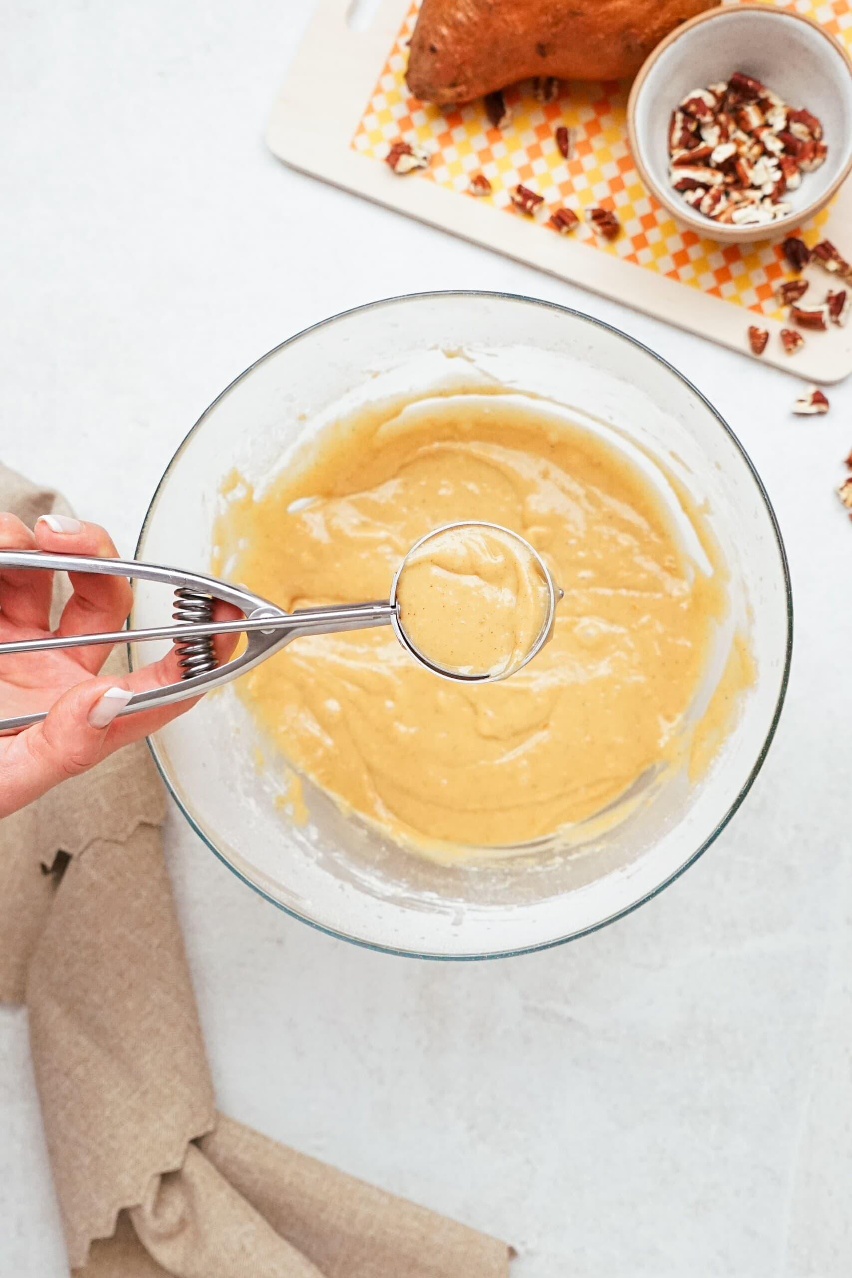 womans hand holding a cookie scoop full of cupcake batter