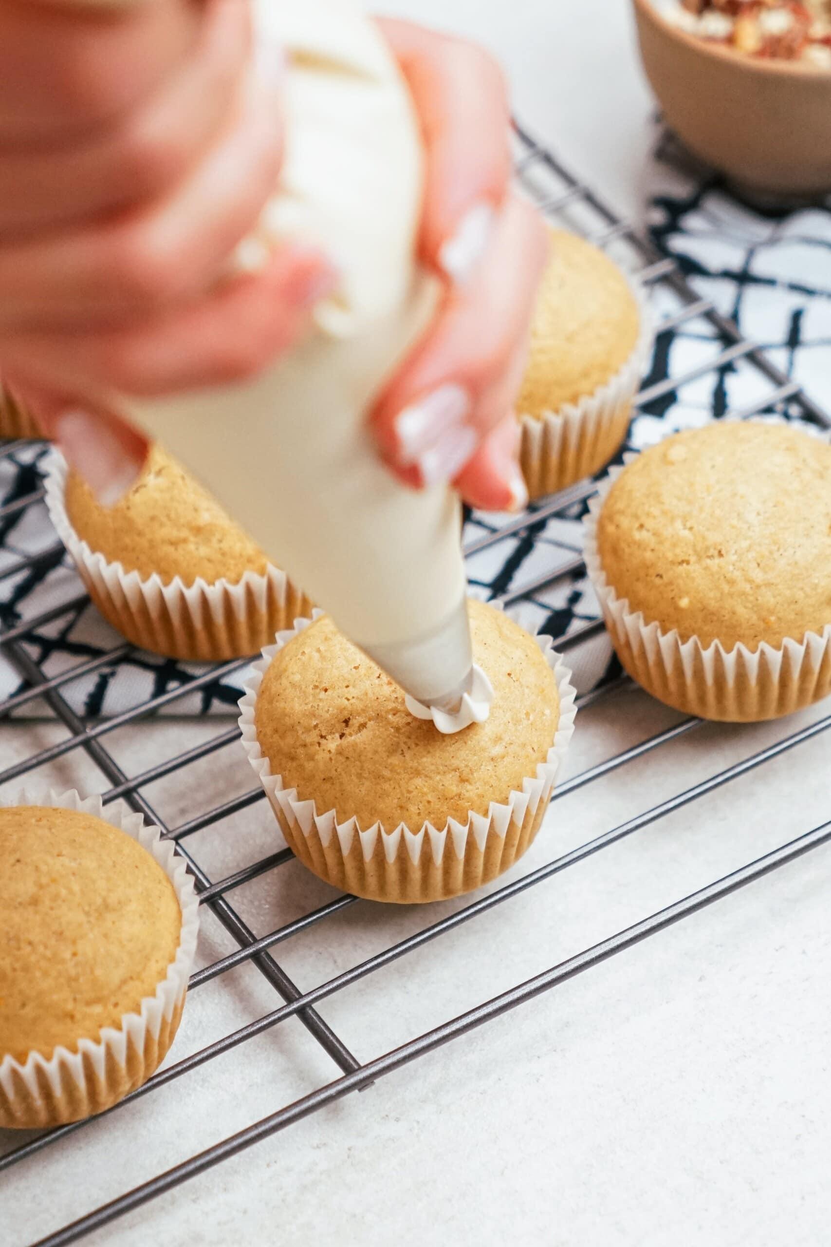 woman's hand piping frosting onto a cupcake