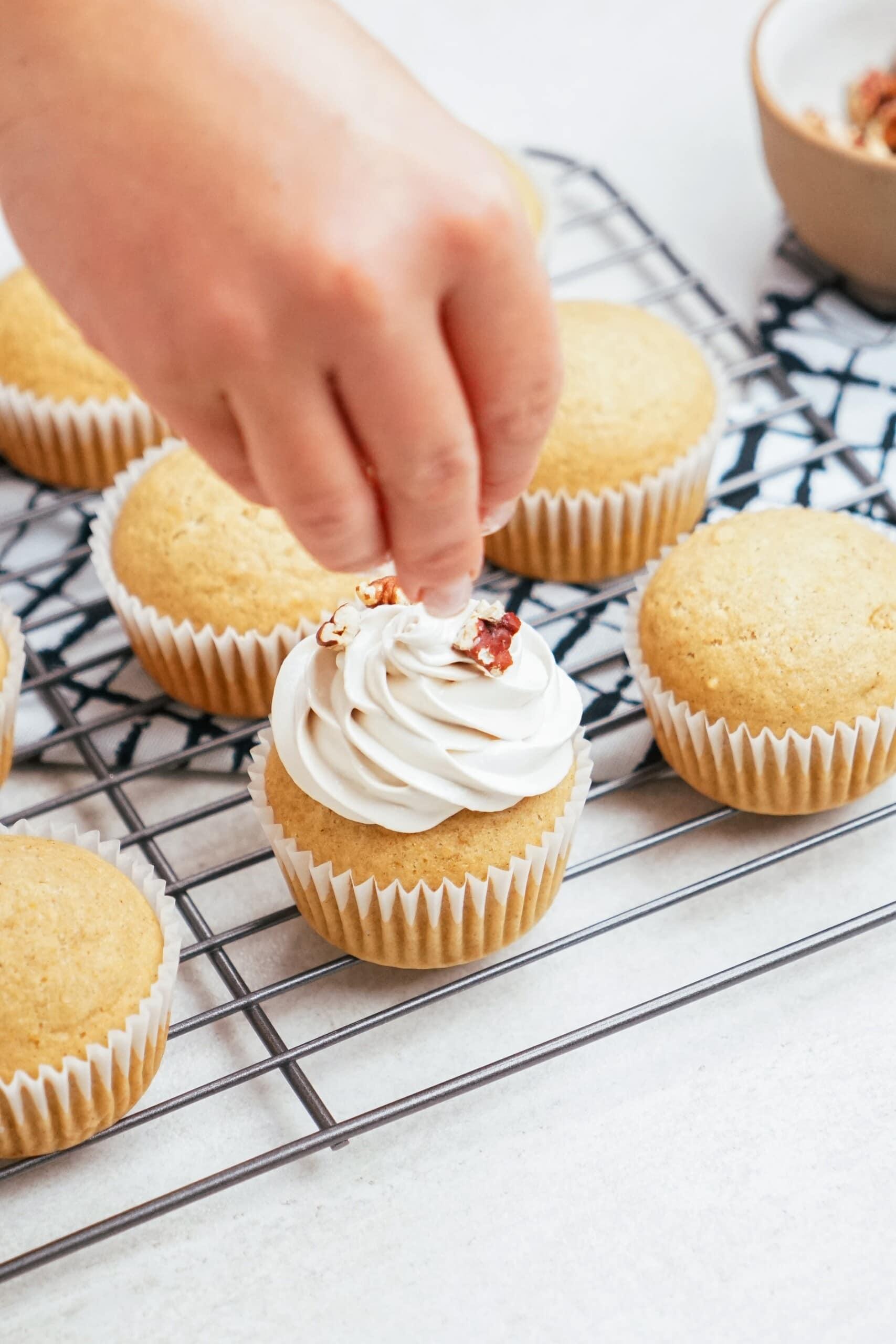 woman's hand adding pecans to the top of a frosted cupcake