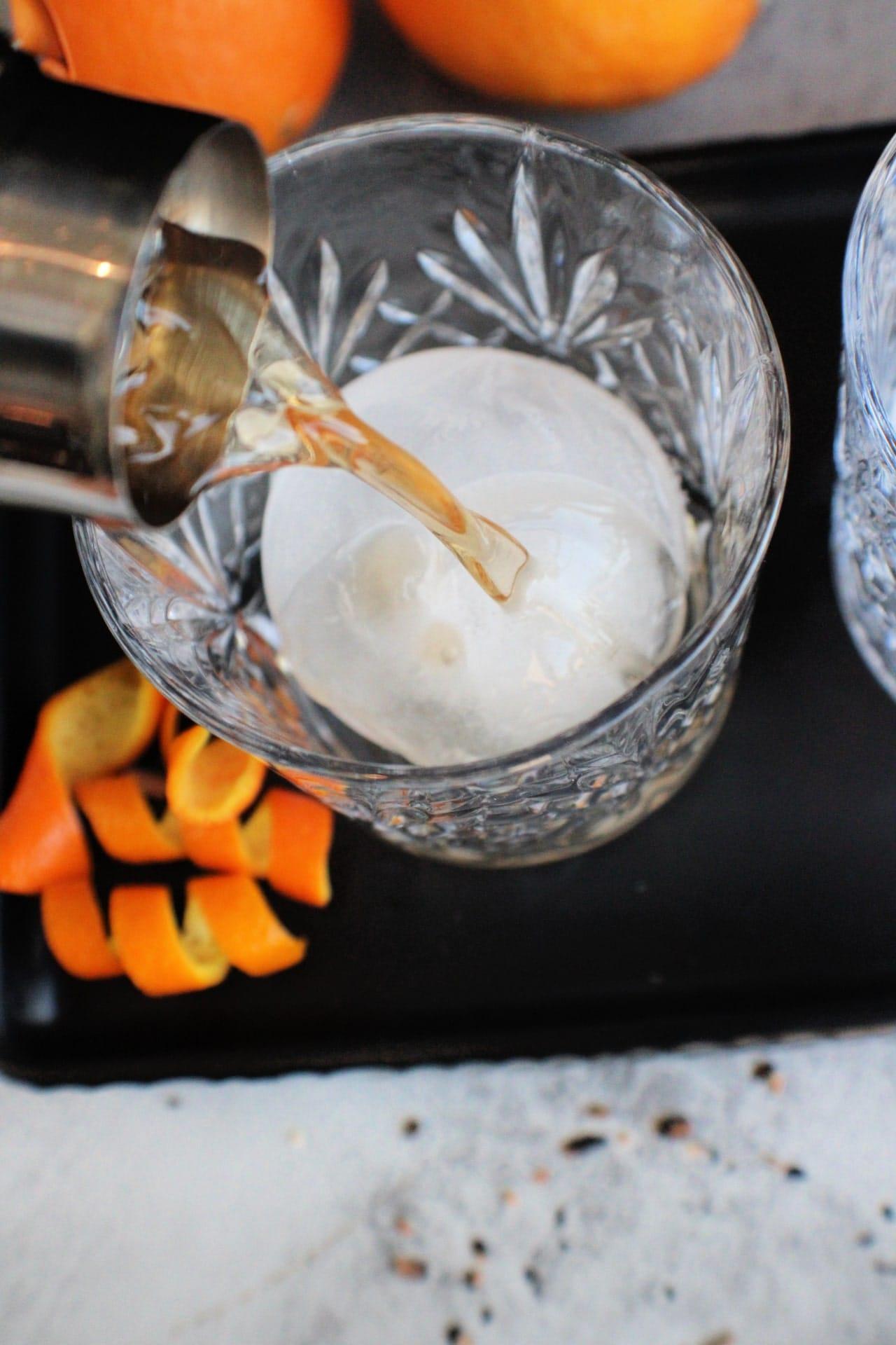 bourbon being poured in a glass over ice