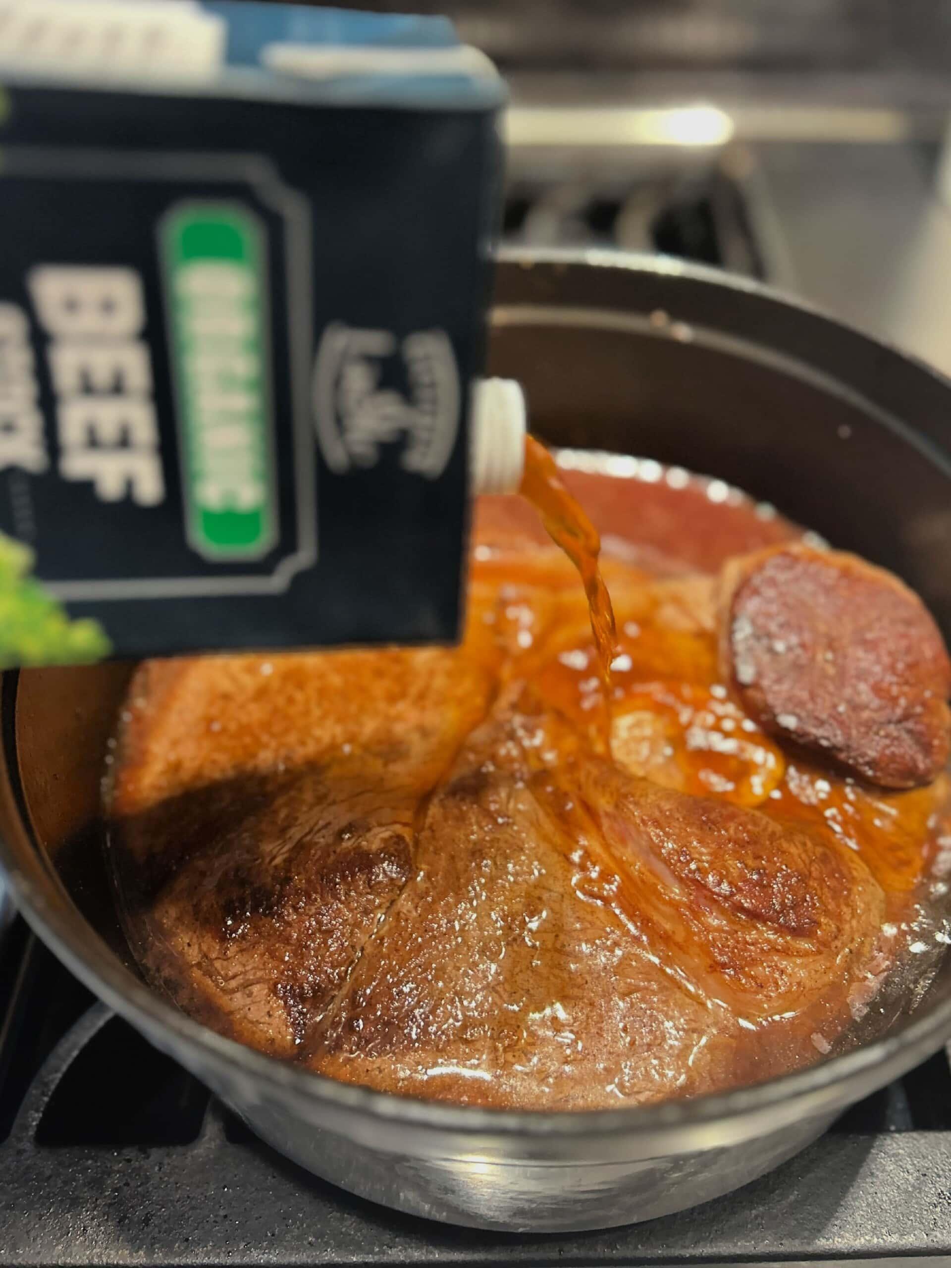 pouring in beef broth to roast in dutch oven pot