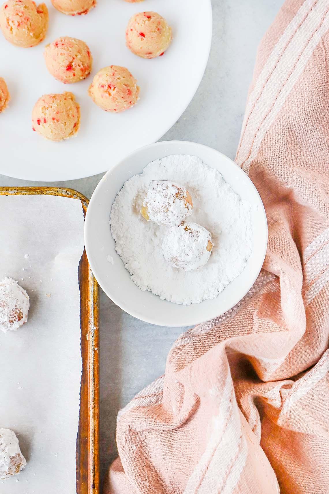 Red Hot Cookies dough balls rolled in bowl of powdered sugar