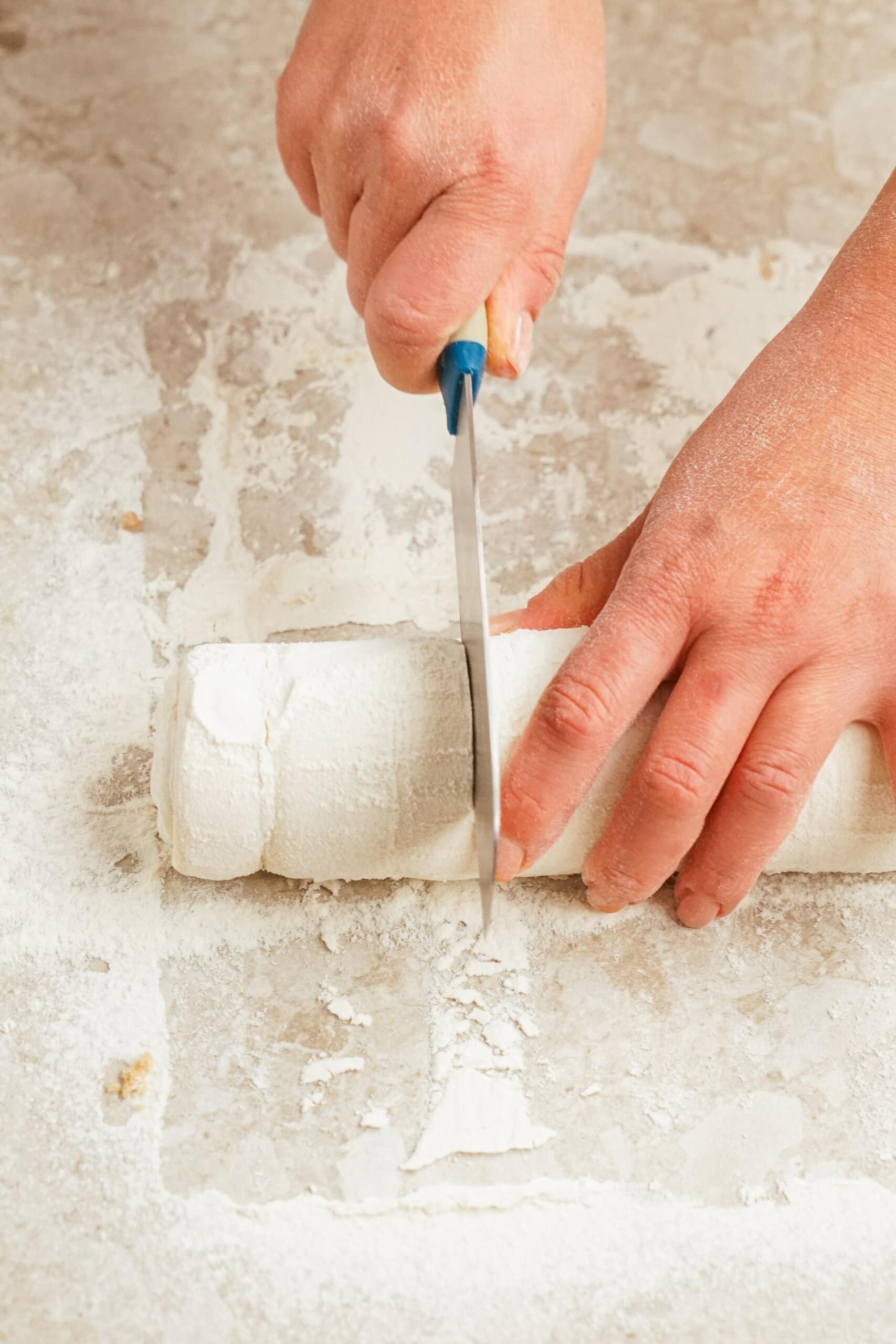 Woman's hands cutting rolled up Puff Pastry sheet with brown sugar and cinnamon mixture