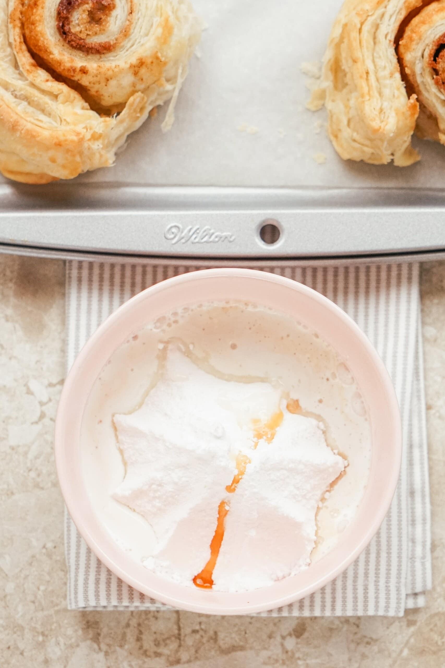 baked unbaked Puff Pastry Cinnamon Rolls on baking sheet with bowl of icing next to it