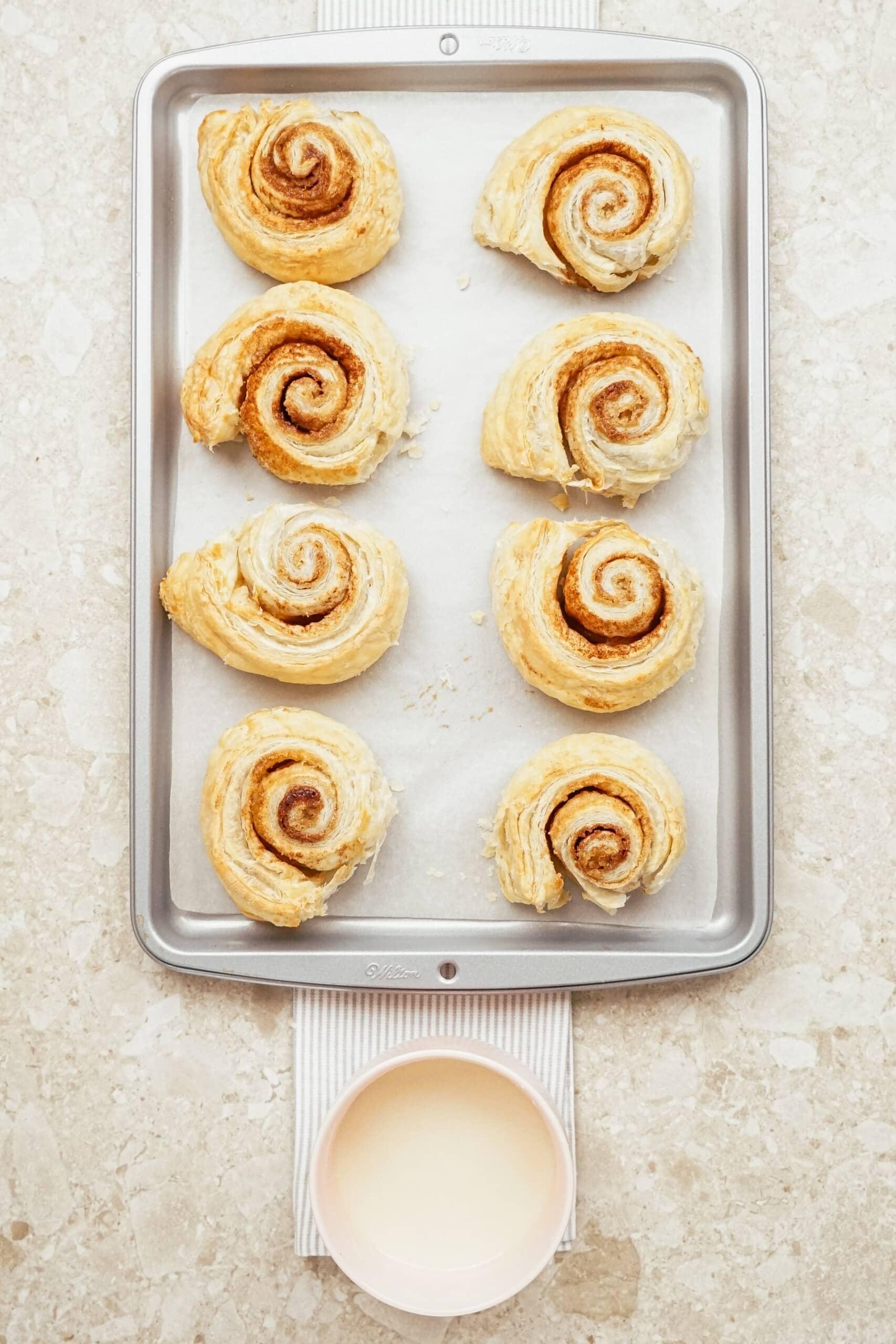 baked cinnamon rolls on baking sheet with bowl of icing next to it