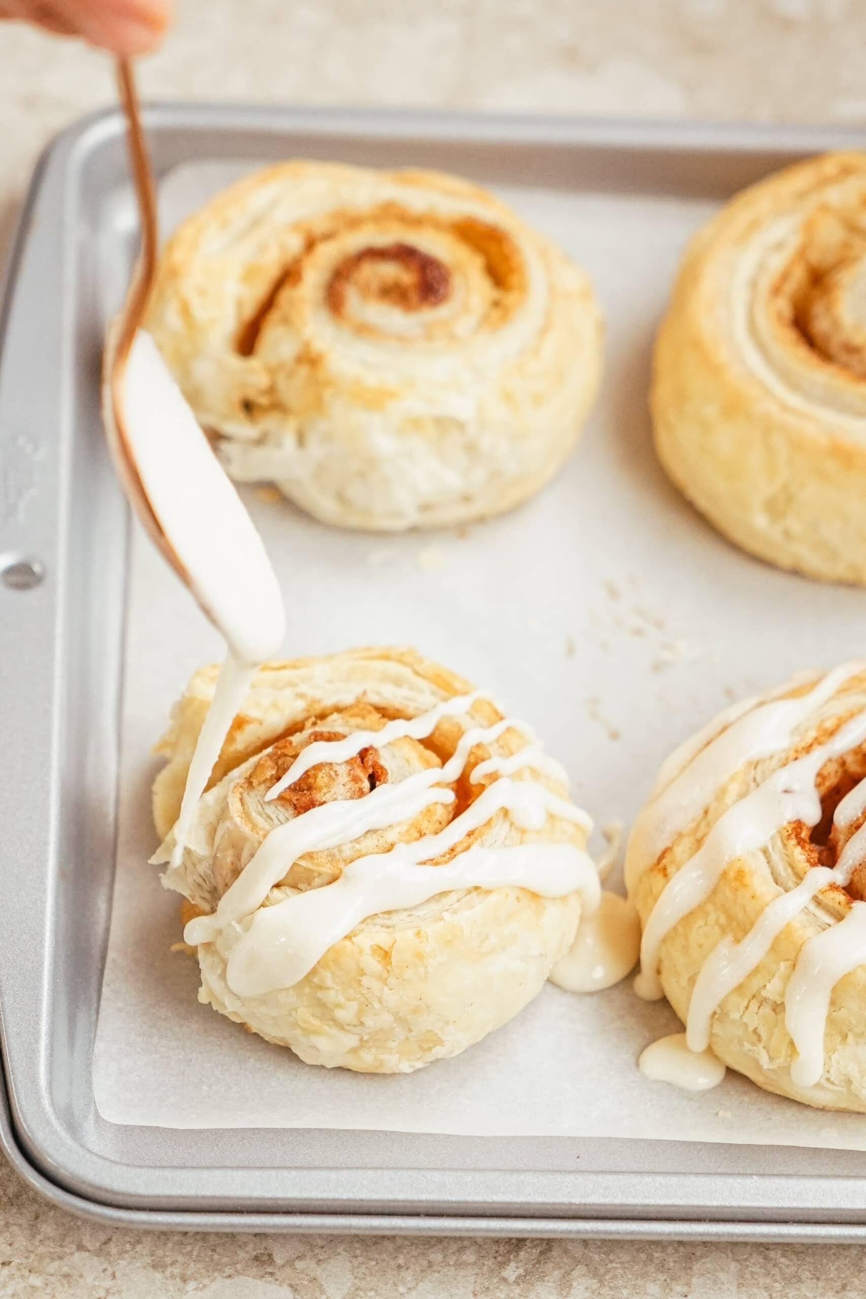 woman's hand drizzling icing on cinnamon rolls on baking sheet with a spoon