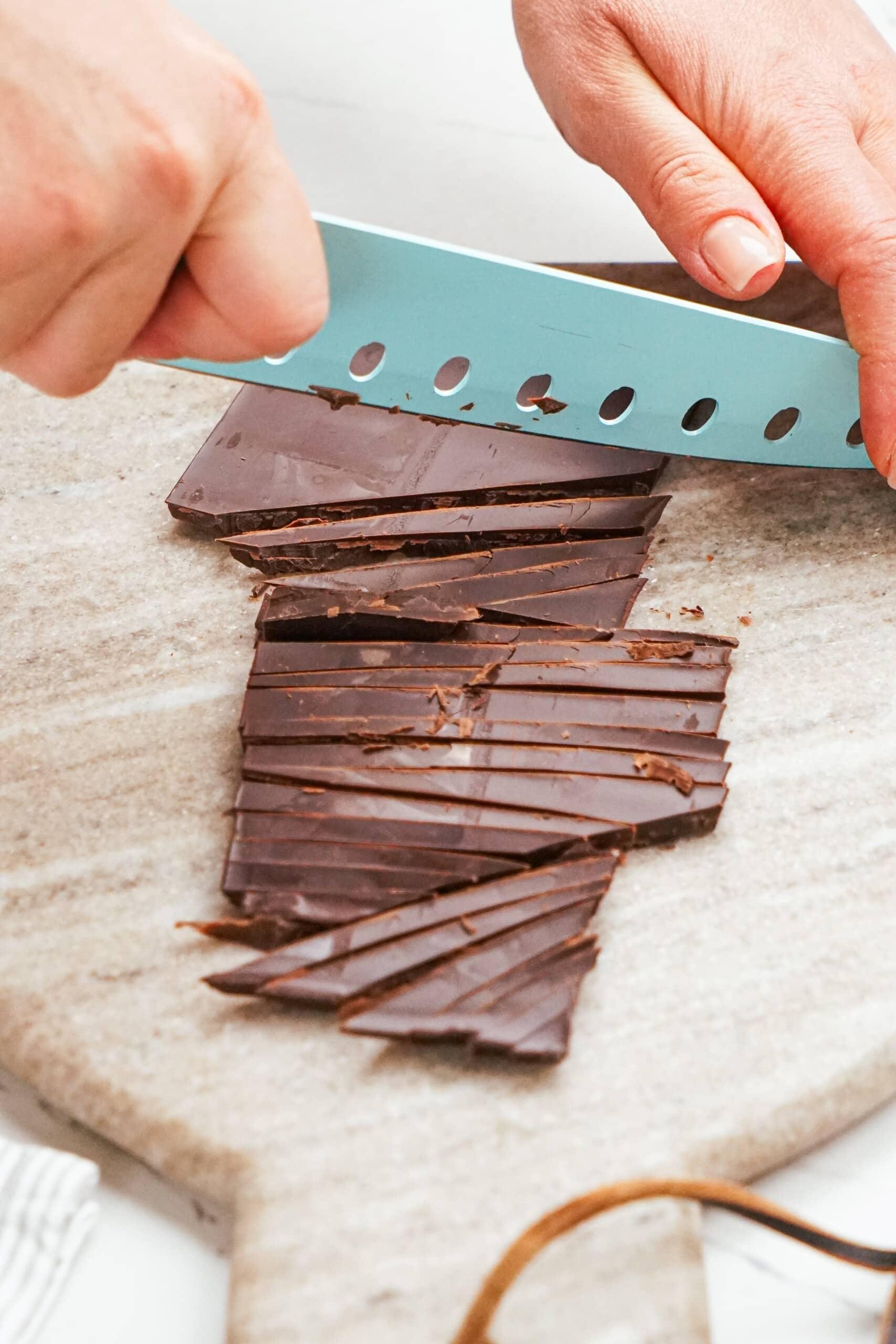 woman's hands chopping chocolate bar with blue kife.