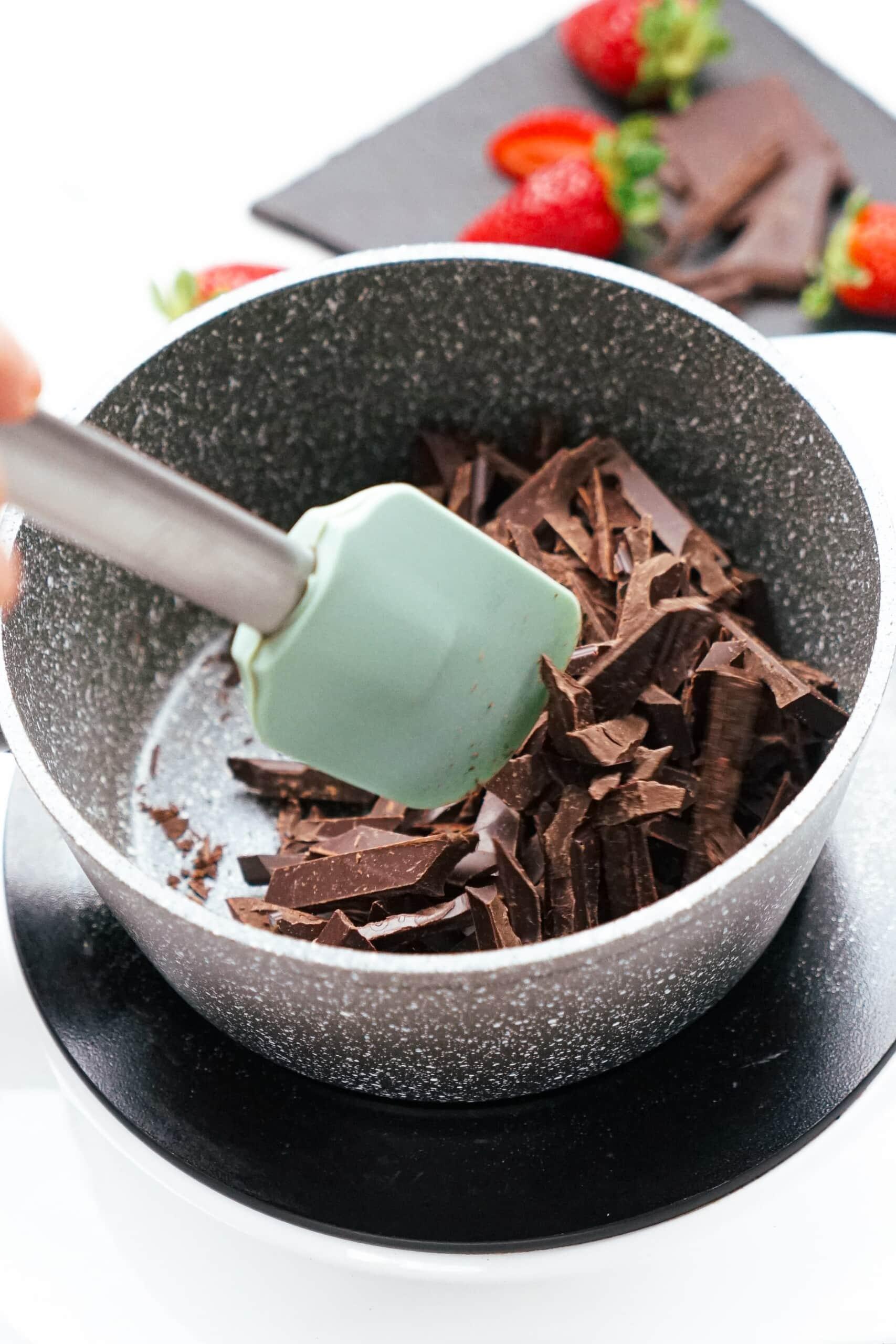 chopped chocolate melting in sauce pot with green rubber spatula stirring.