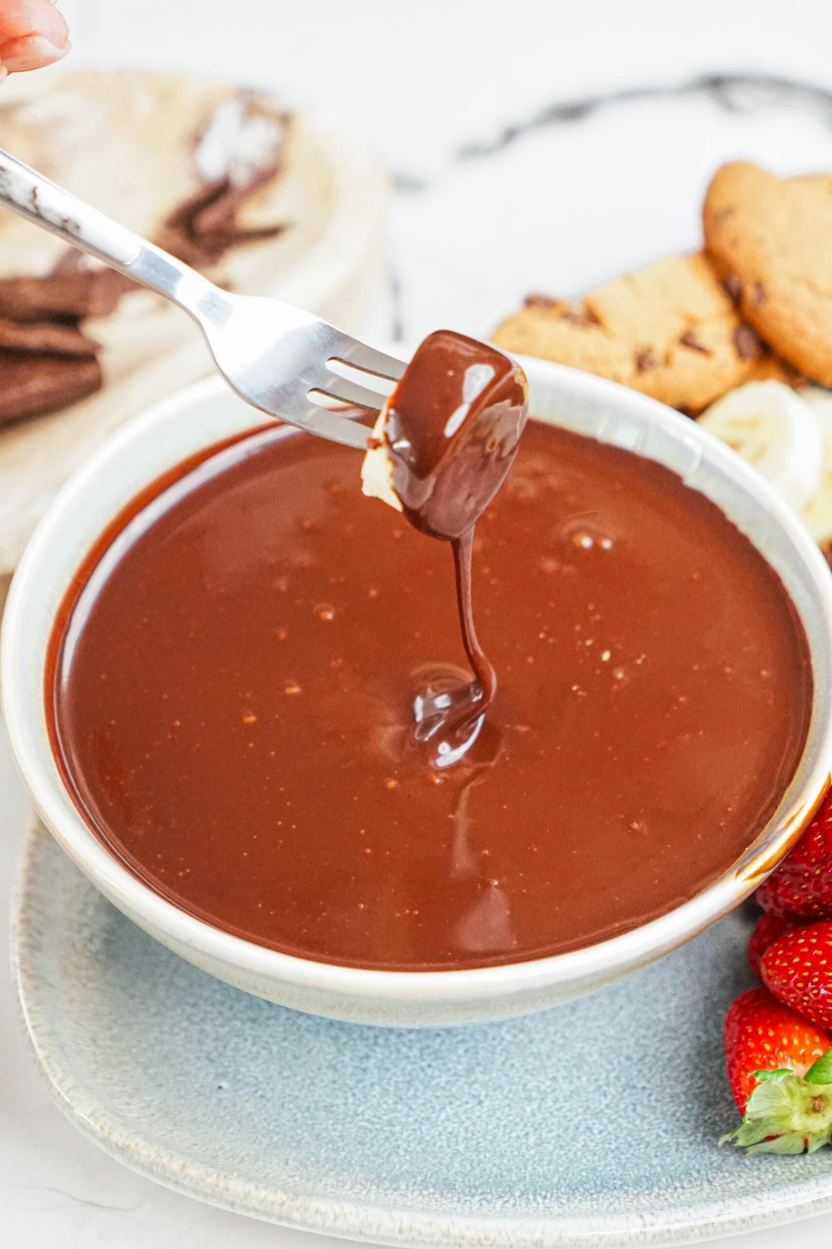 fork with piece of banana being dipped into a bowl of chocolate.