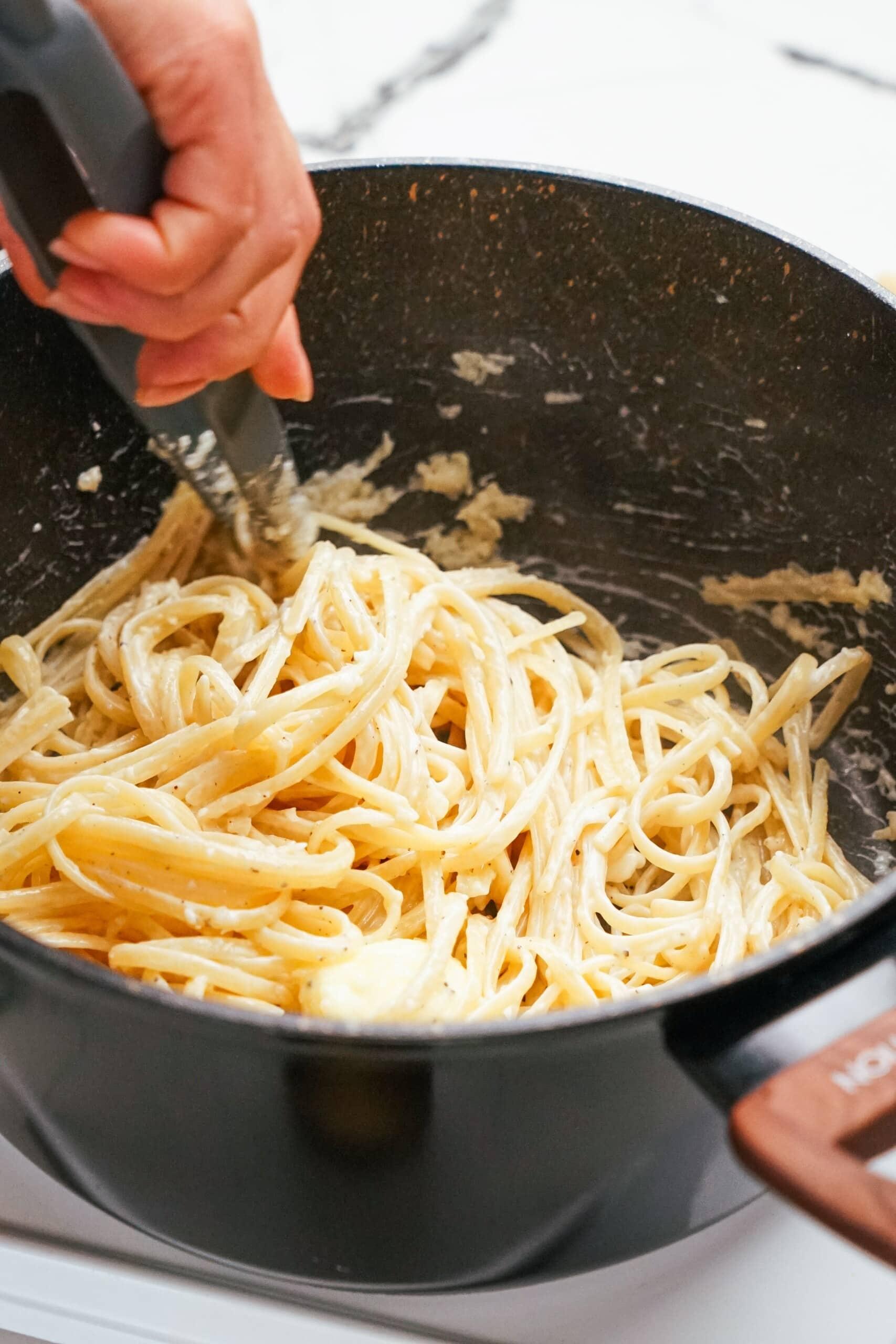 parmesan garlic linguine recipe in pot with woman's hand using tongs