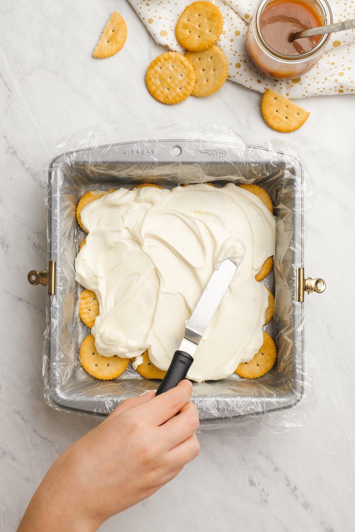 womans hand spreading cream cheese mixture across ritz crackers