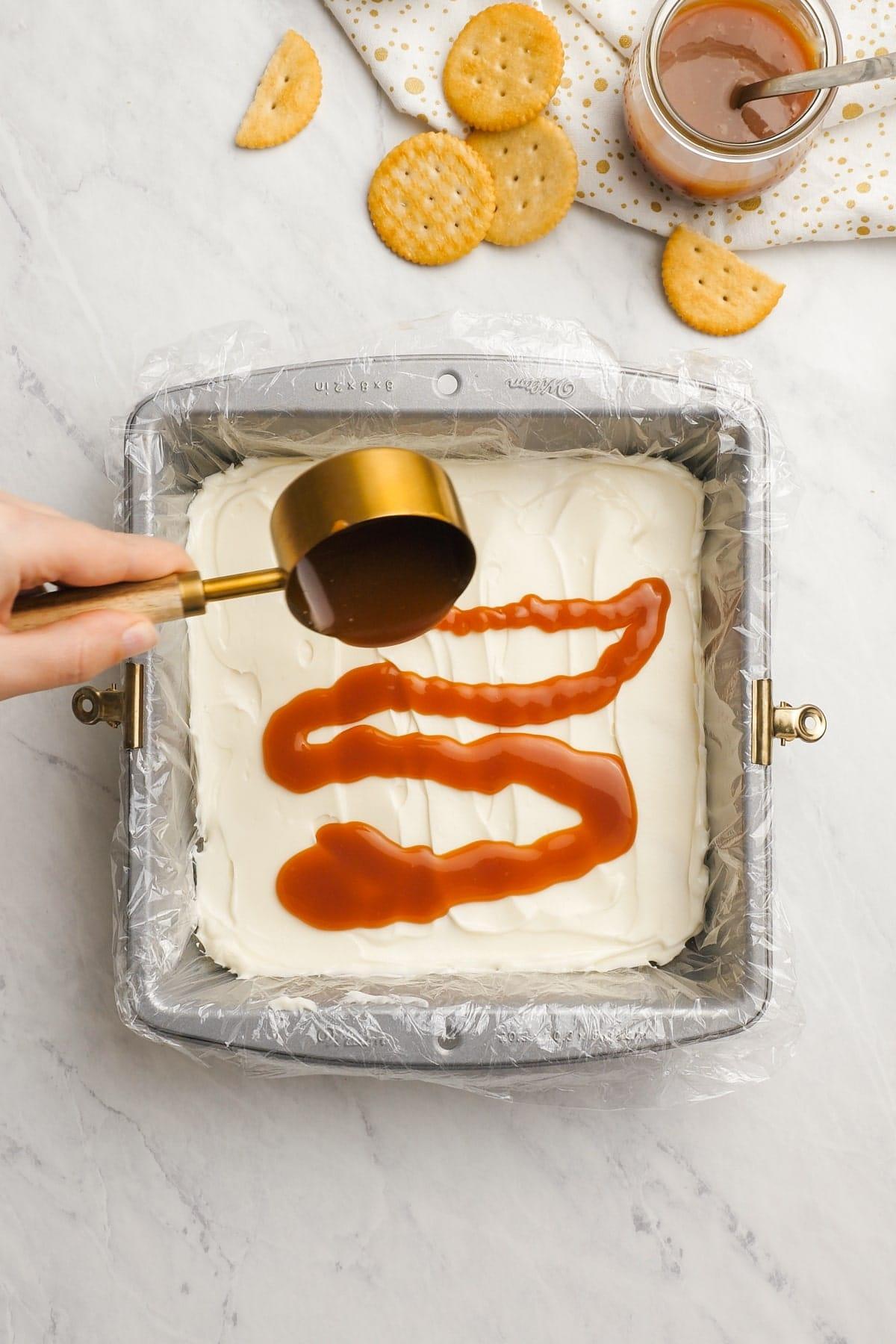 woman's hand pouring salted caramel sauce over cream cheese layer