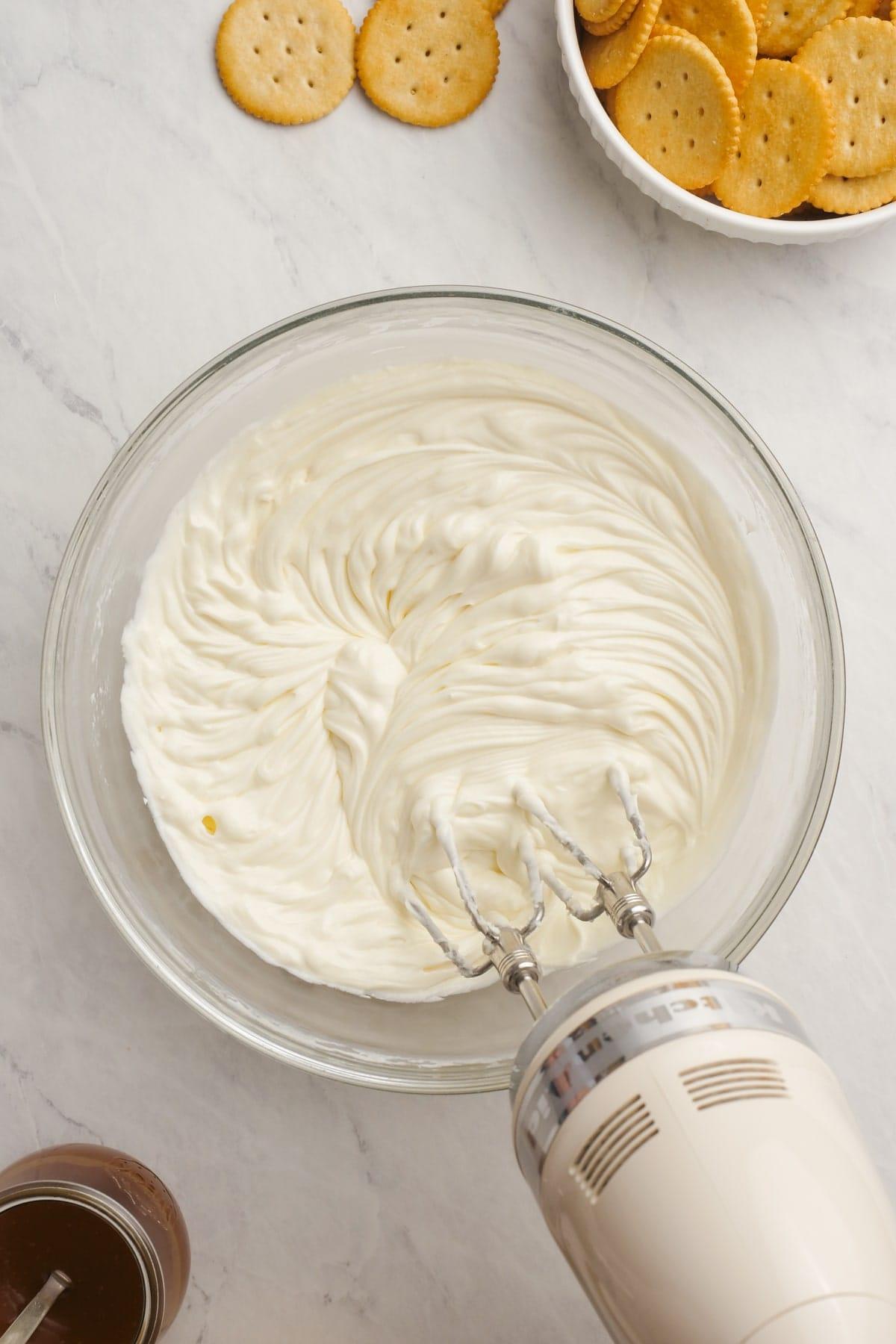 hand mixer mixing cream cheese and sugar together in a bowl