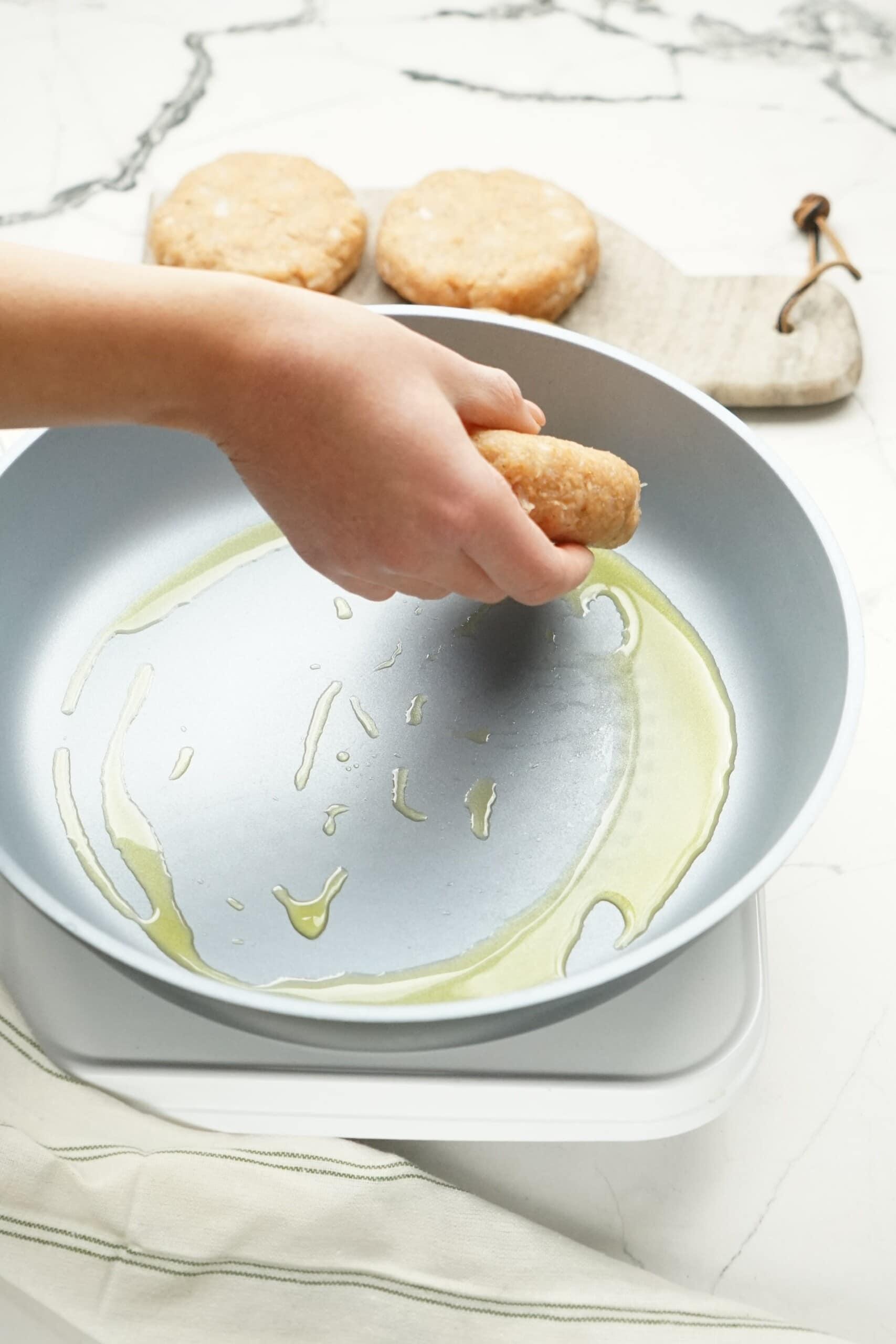 woman's hand placing meat patty into a hot, oiled skillet