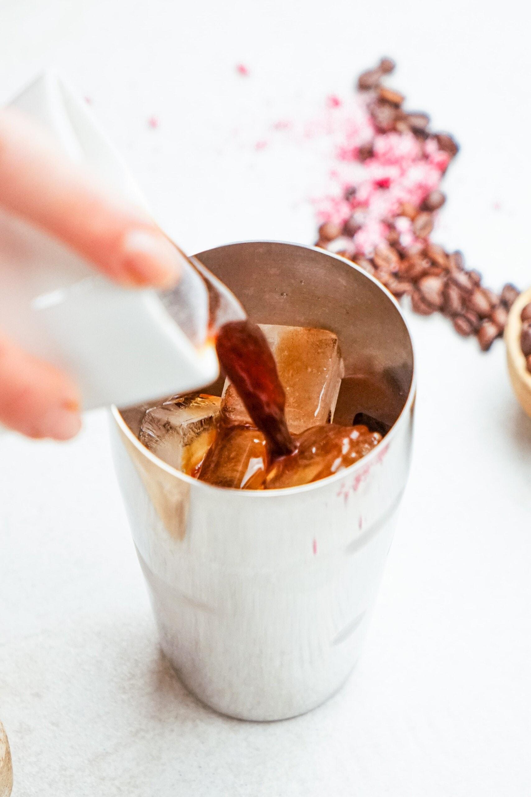 pouring espresso into a cocktail shaker with ice cubes