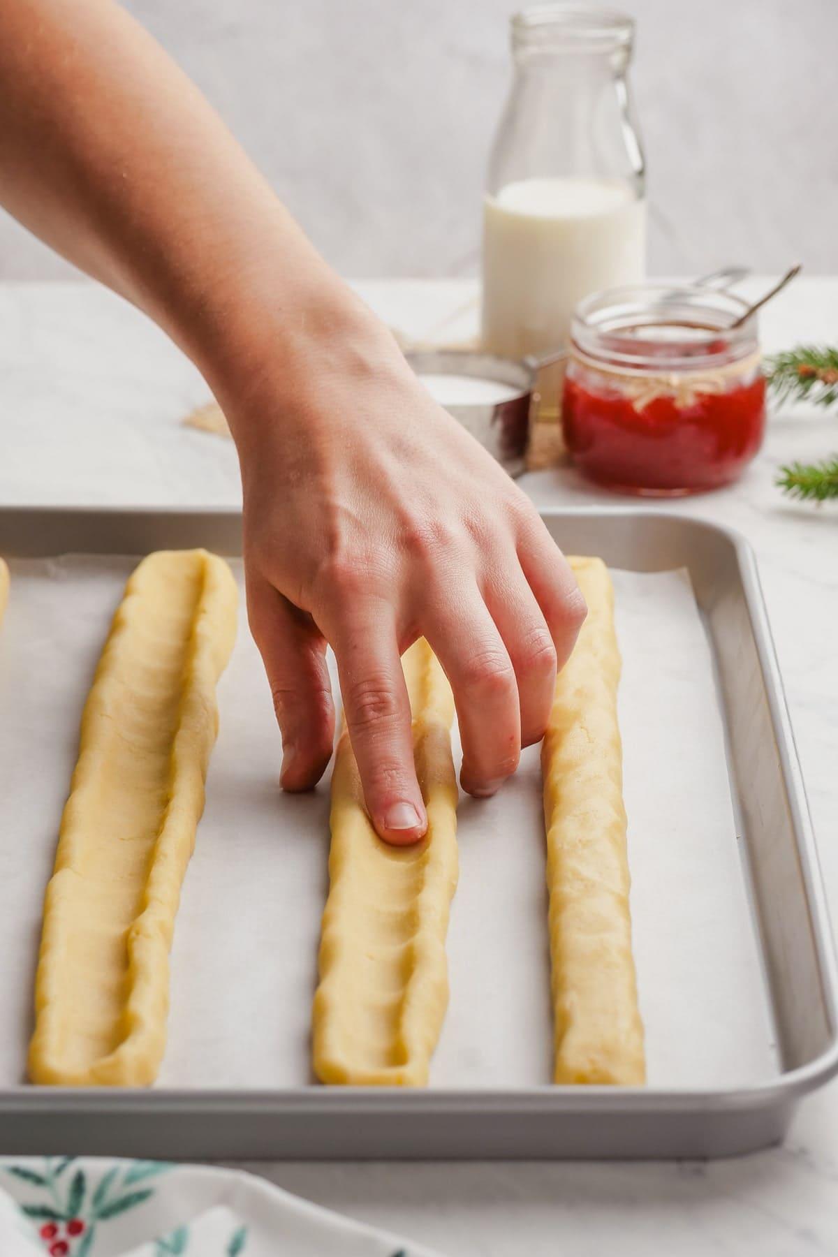  shortbread dough on baking sheet with womans hand creating a well down the center of each log 