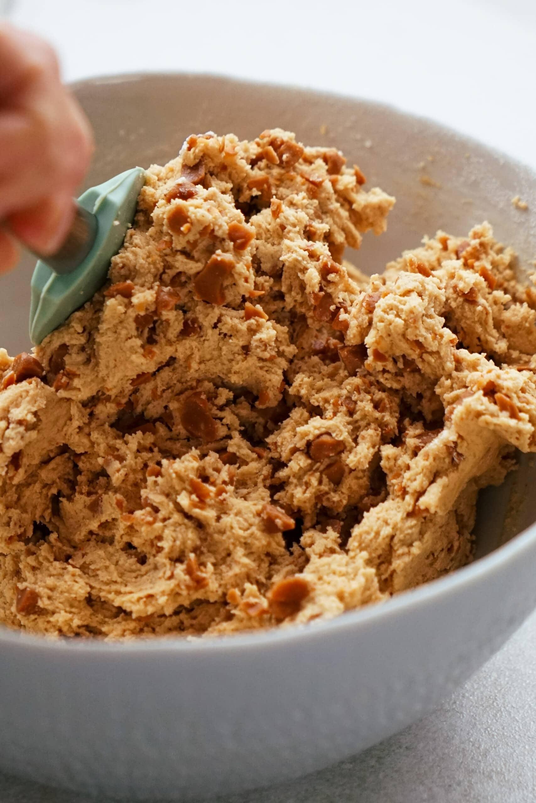 rubber scrapper mixing toffee bits into dough