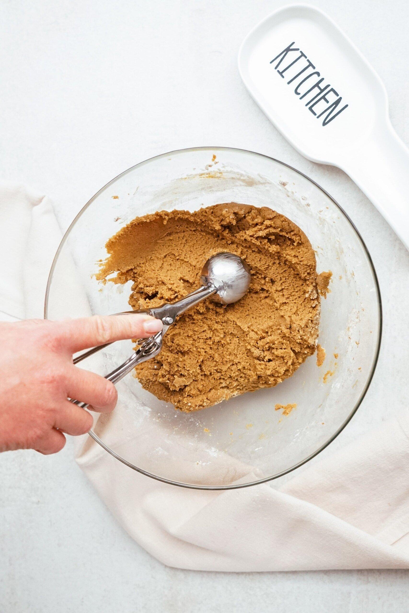 womans hand scooping dough with a cookie scoop