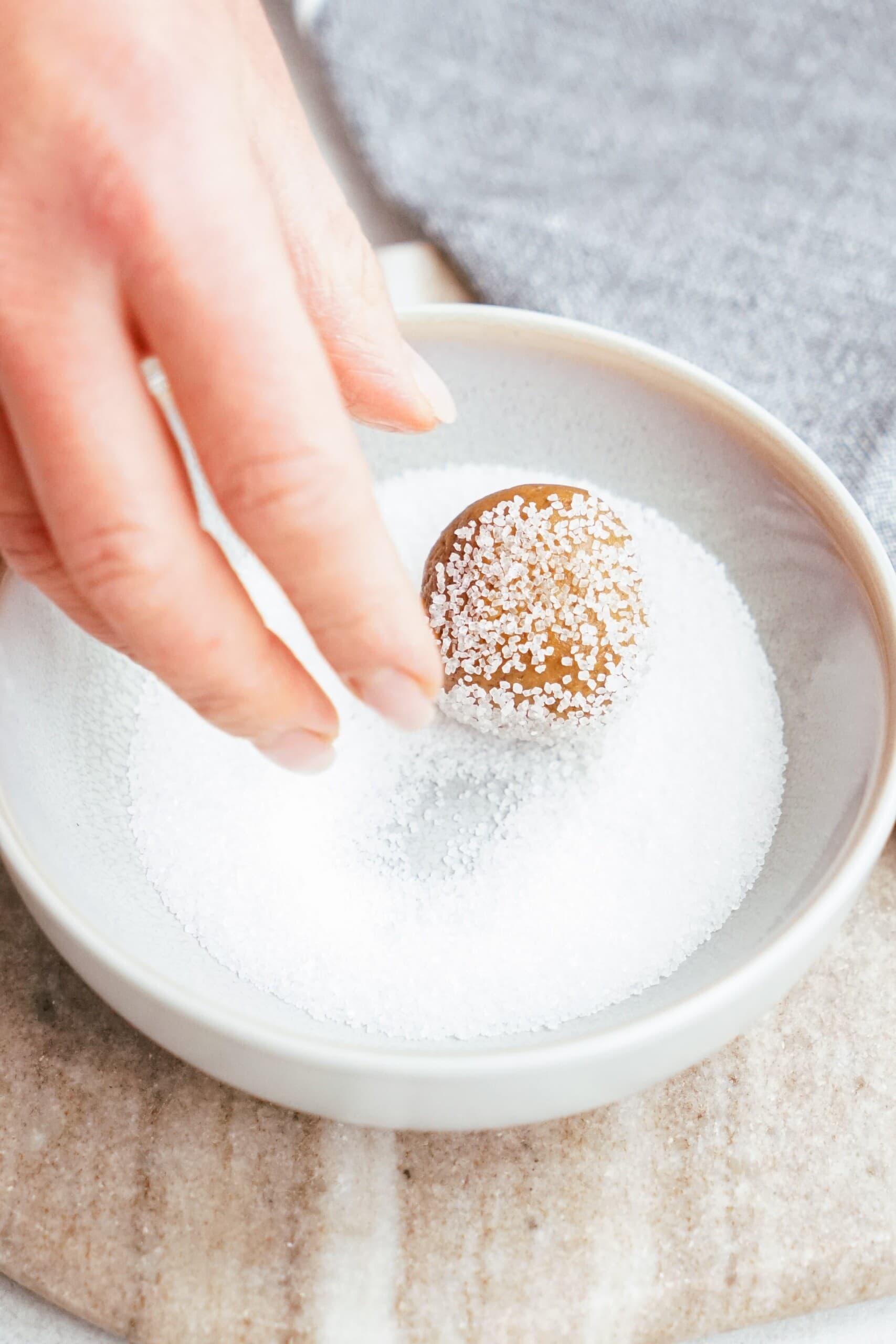 womans hand rolling cookie dough ball in sugar 