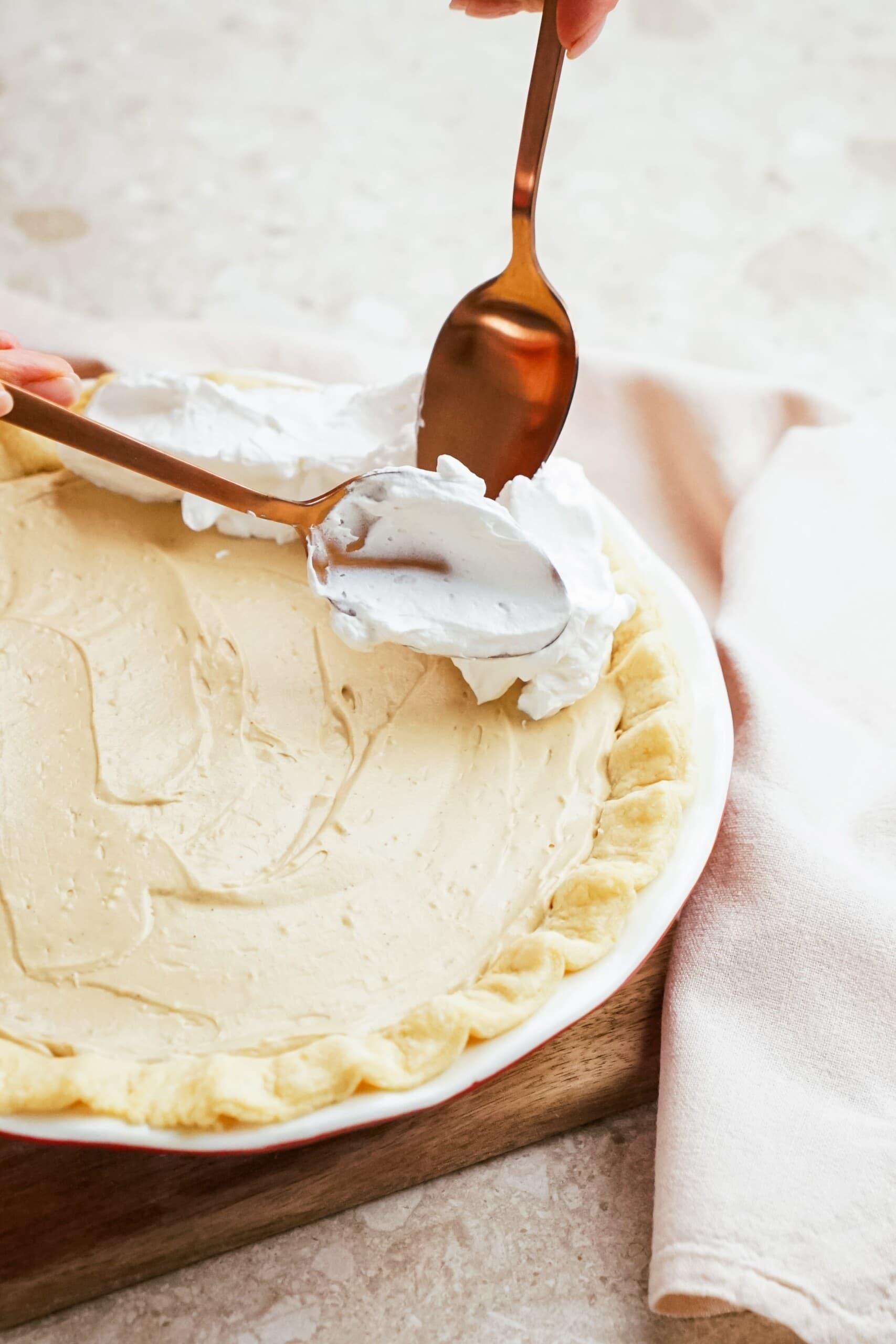 adding whipped cream to the edge of a pie with 2 gold spoons