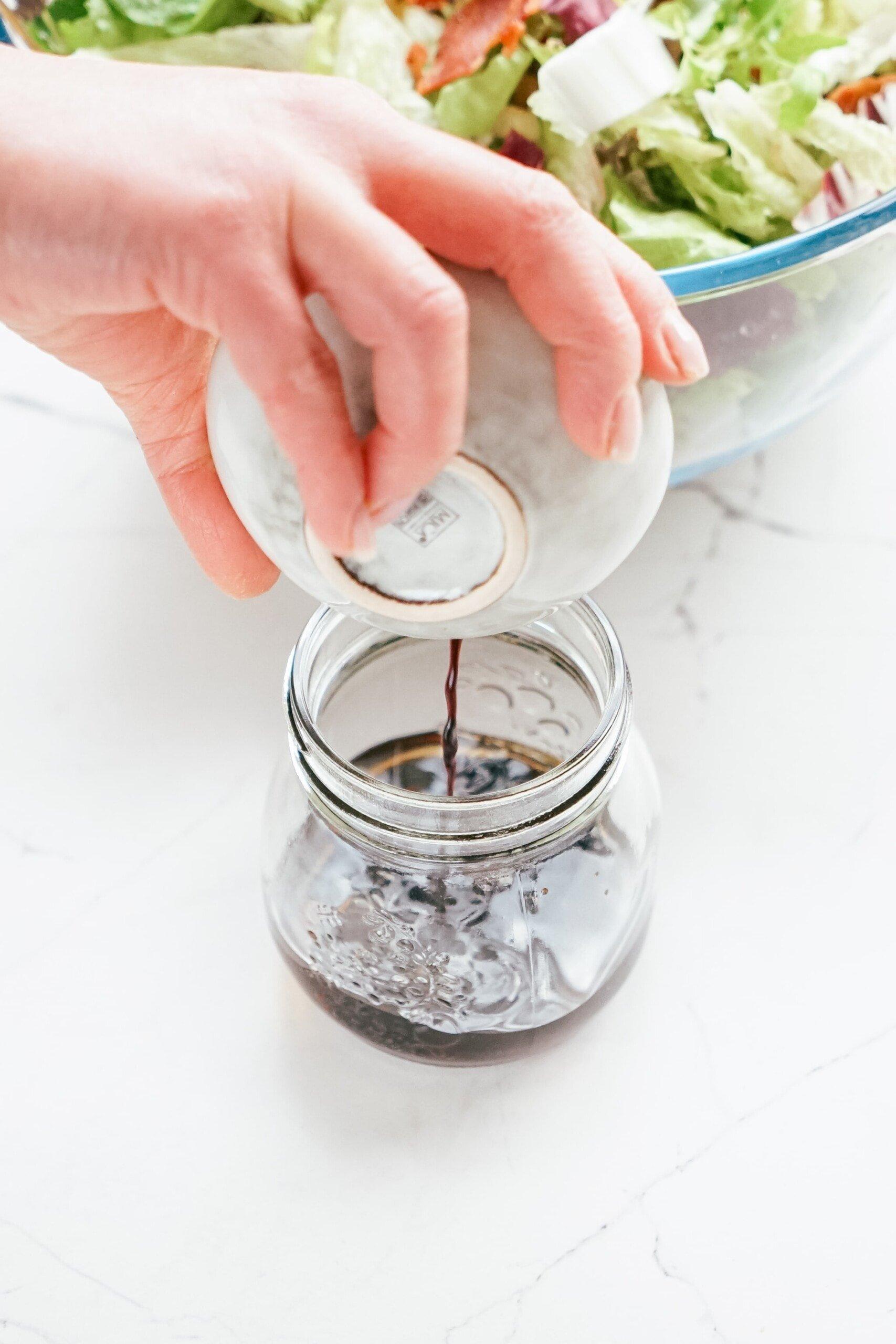 womans hand adding balsamic vinegar to a jar 