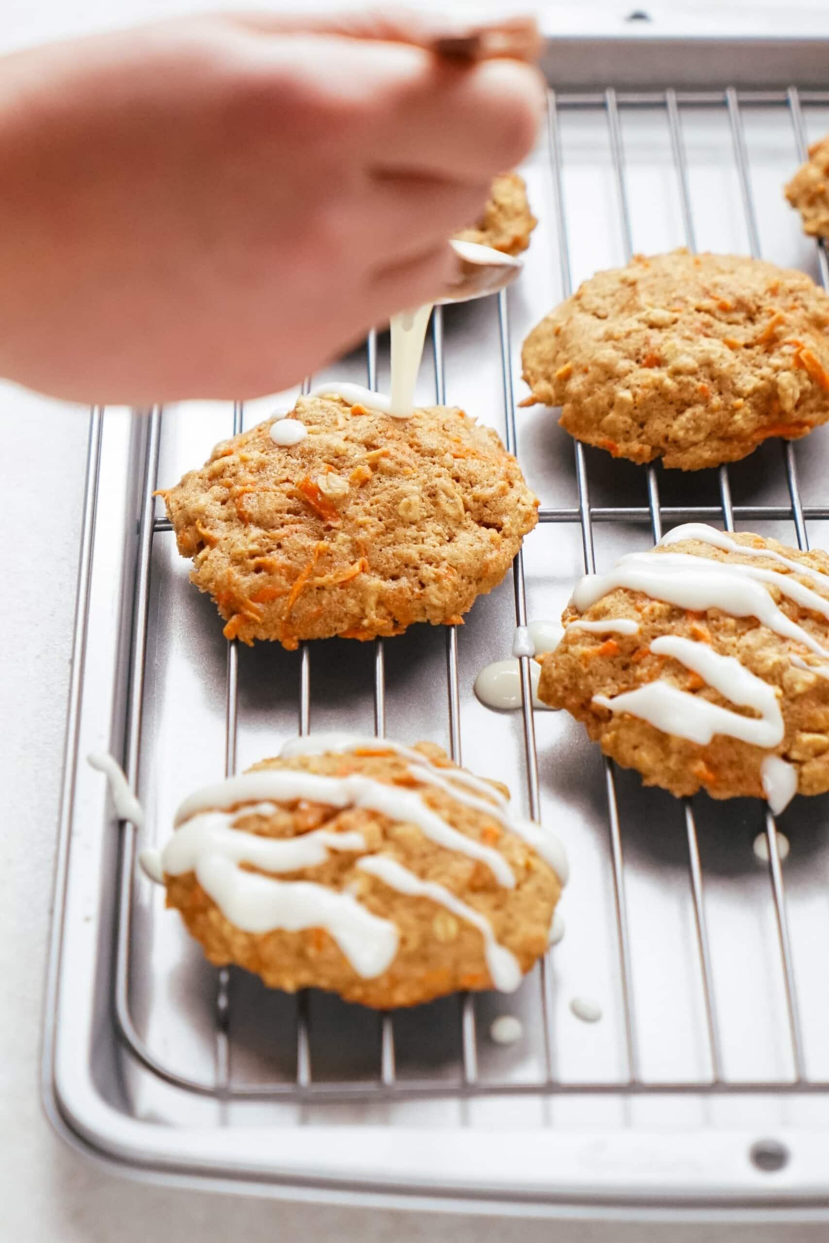 woman's hand drizzling glaze over warm cookies 