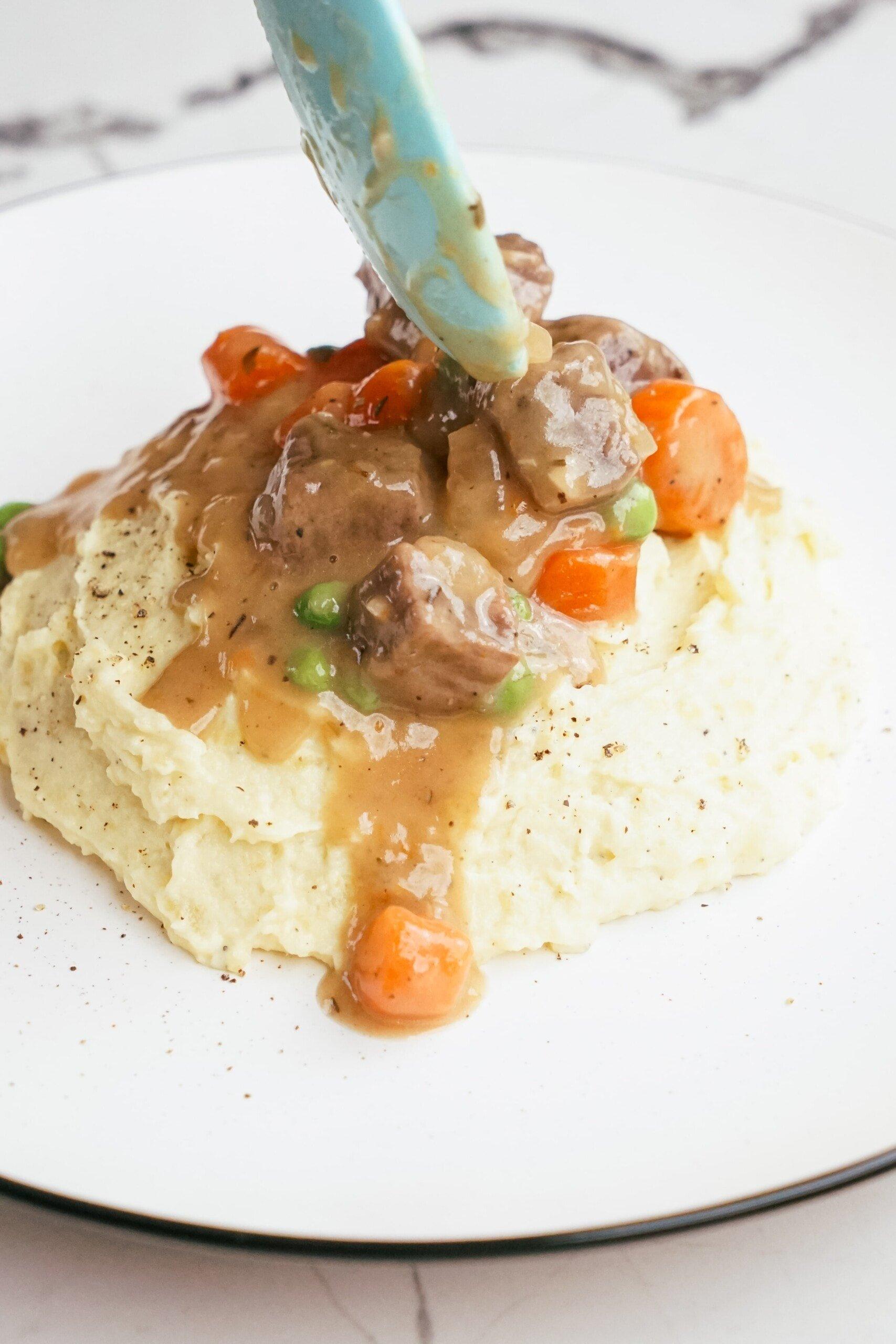 Beef Stew blue spoon serving beef stew over mashed potatoes on plate