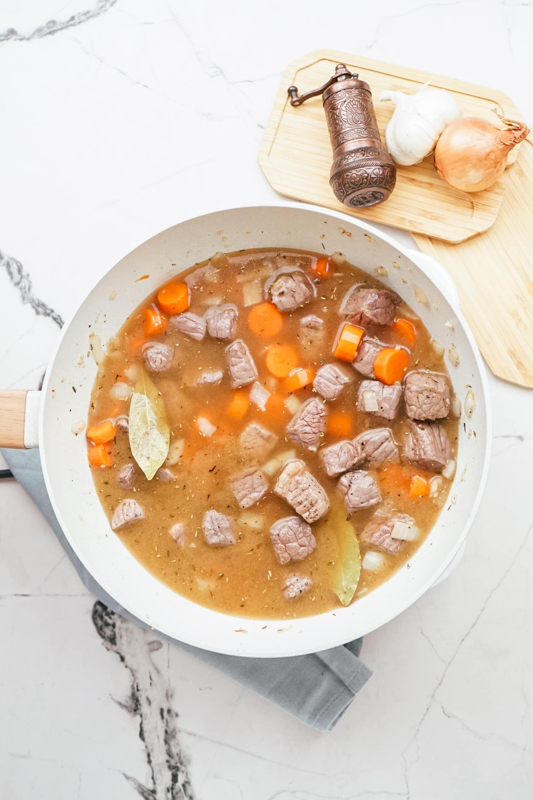 beef stew ingredients cooking in pan of broth