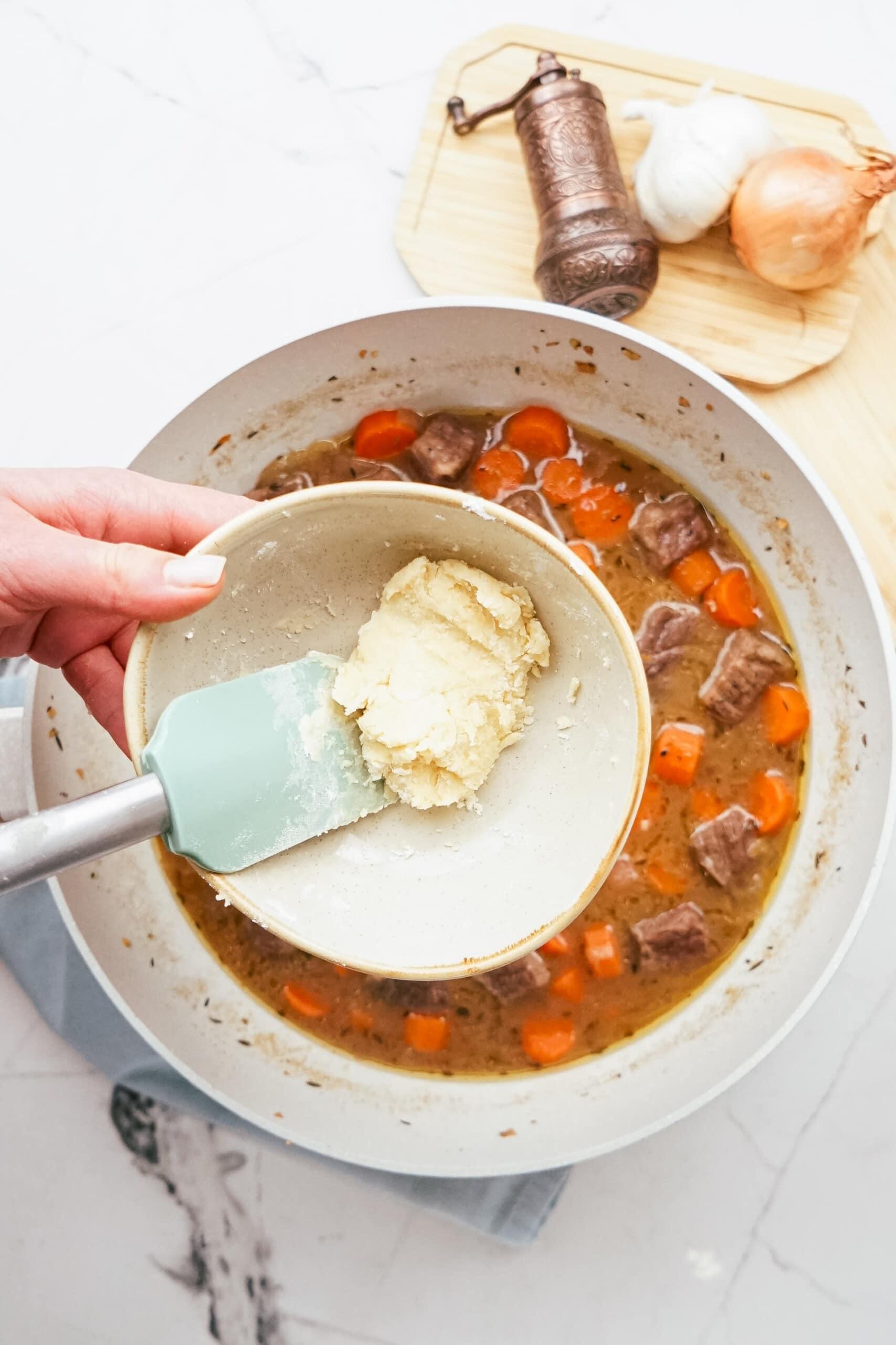 woman's hand adding a roux to a pan of beef stew