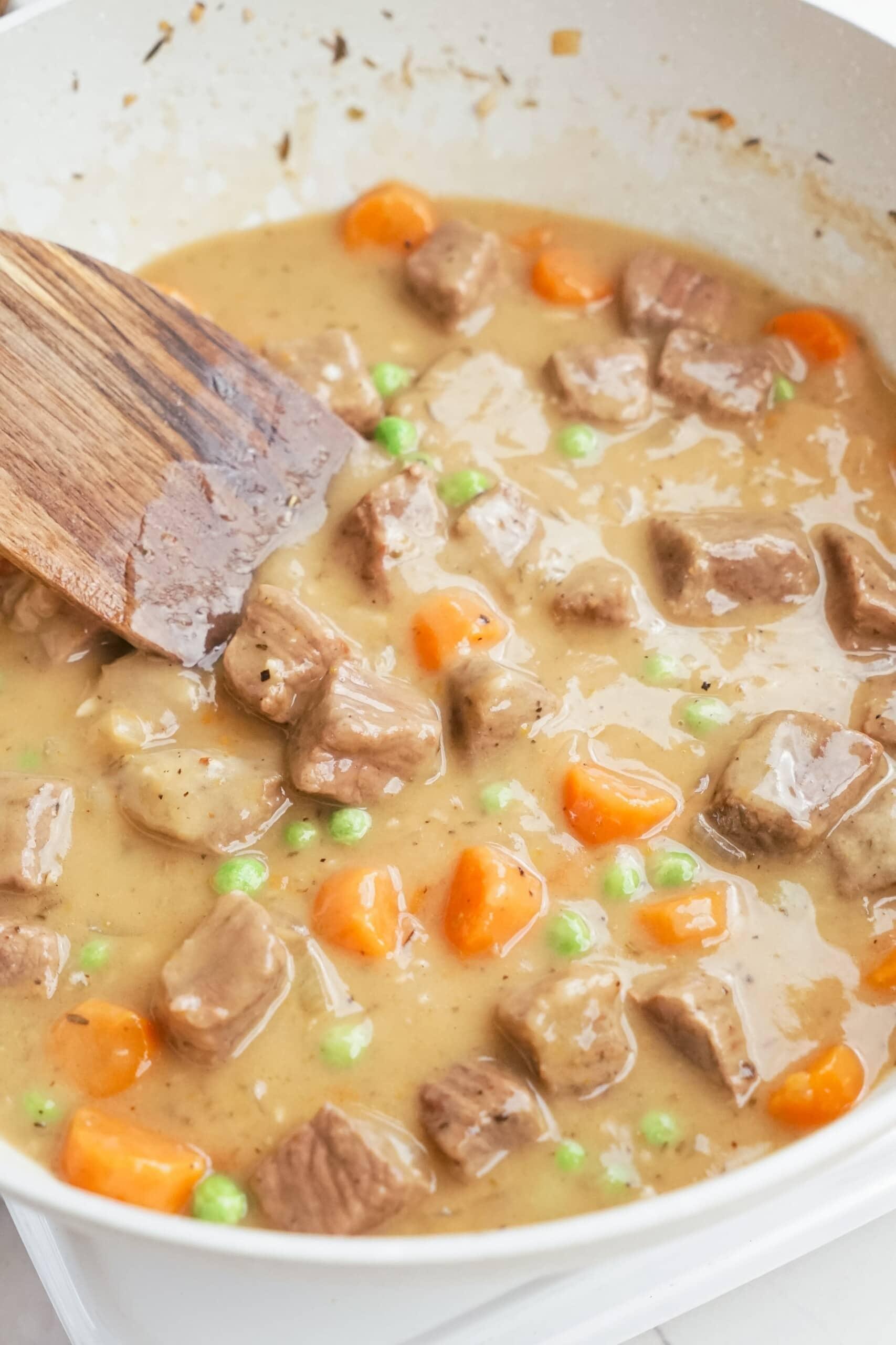 beef stew in pot with wooden spoon stirring