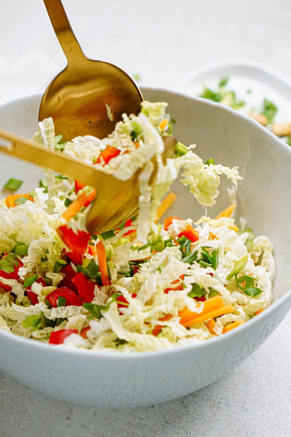 large gold spoons tossing salad ingredients together