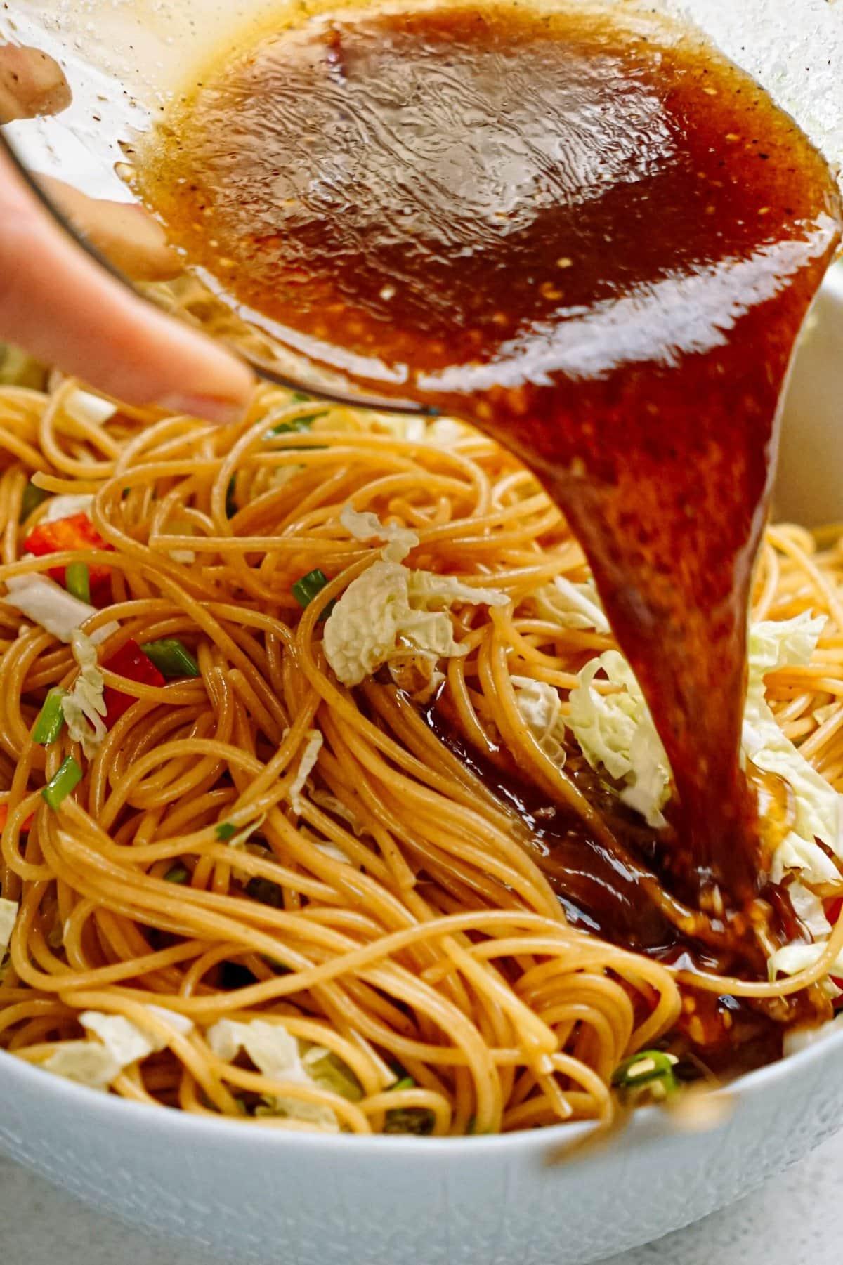 sesame dressing being poured over noodles