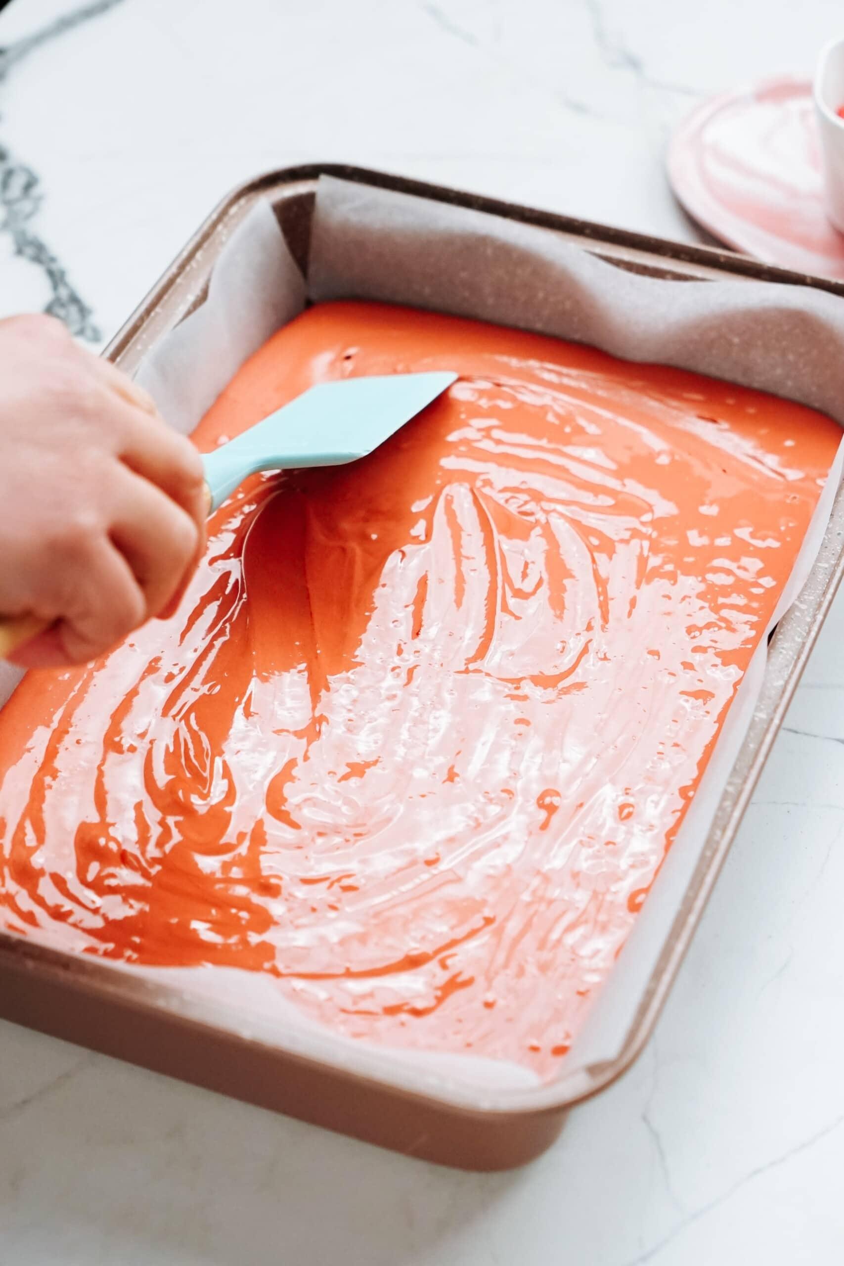 cake batter in a cake pan. womans hand smoothing batter with a rubber spatula 