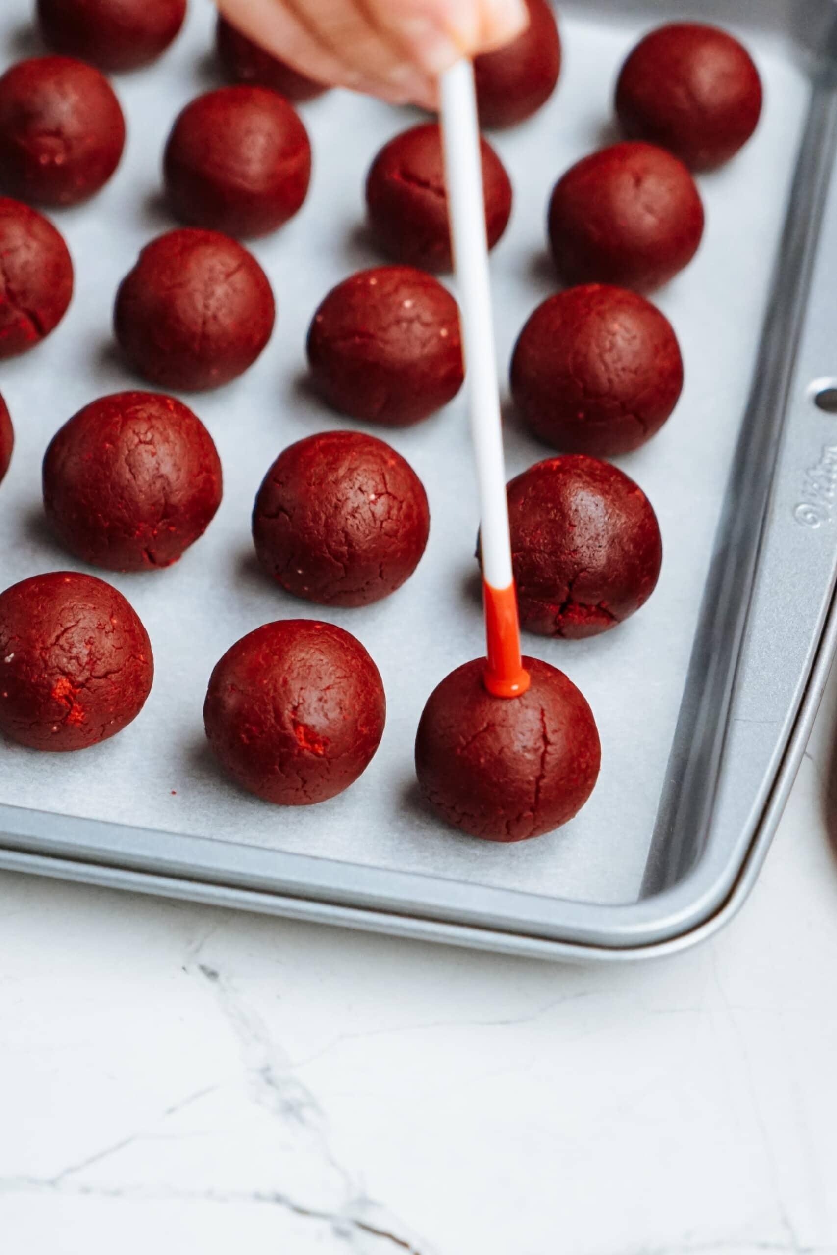 inserting lollipop stick into cake ball on sheet pan 