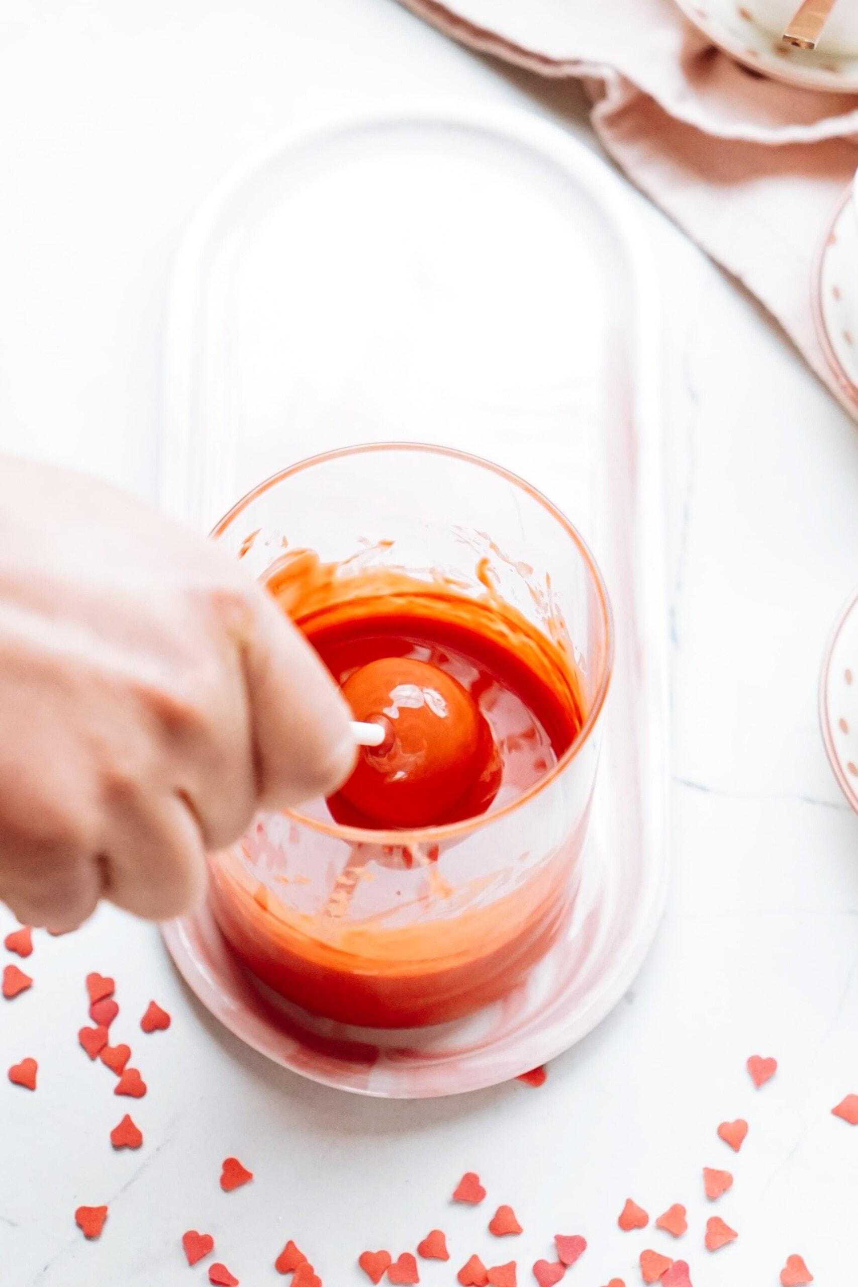 woman's hand dipping cake ball on a stick into melted chocolate 