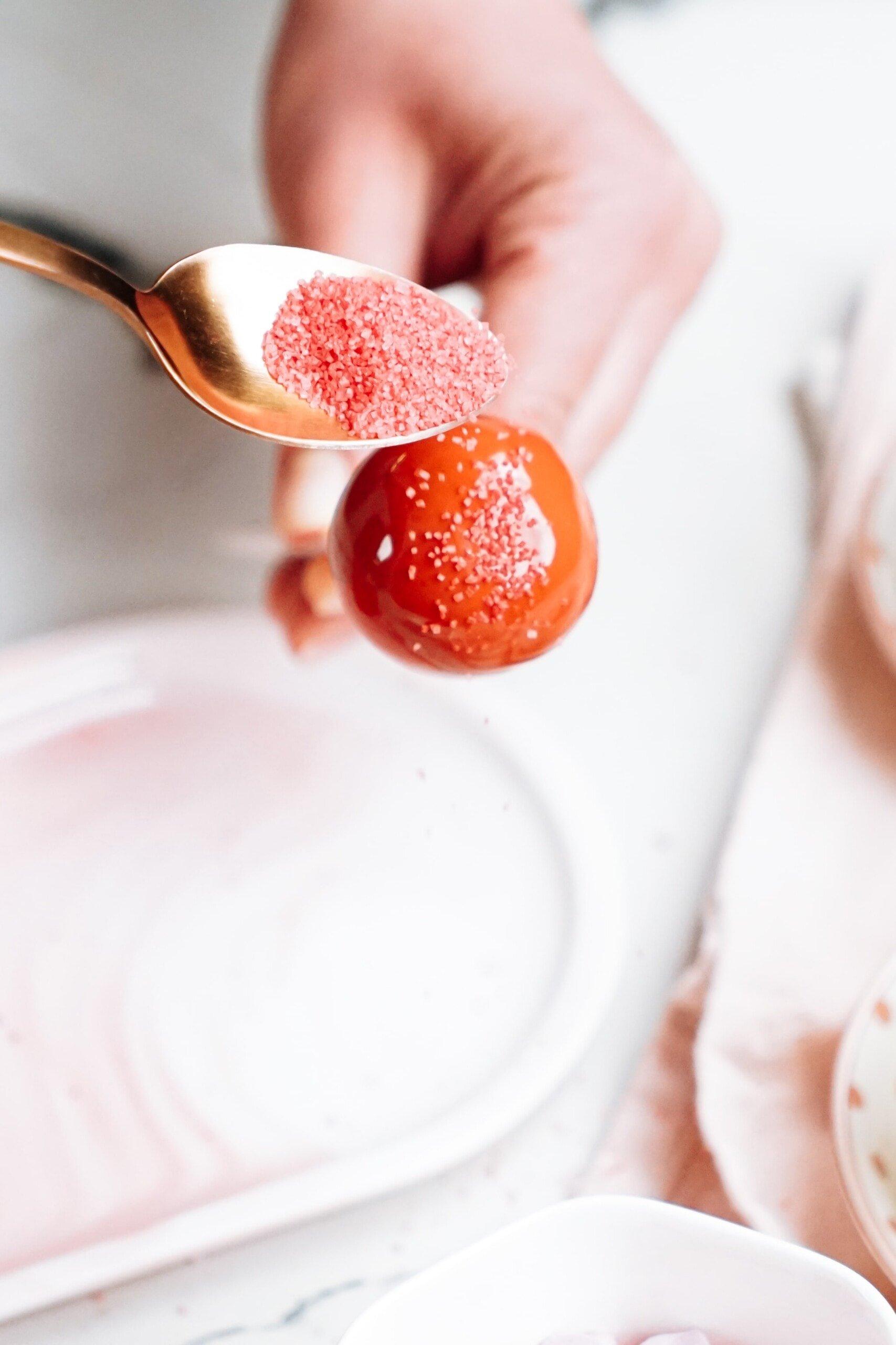 womans hand holding a cake pop while adding sanding sugar to it