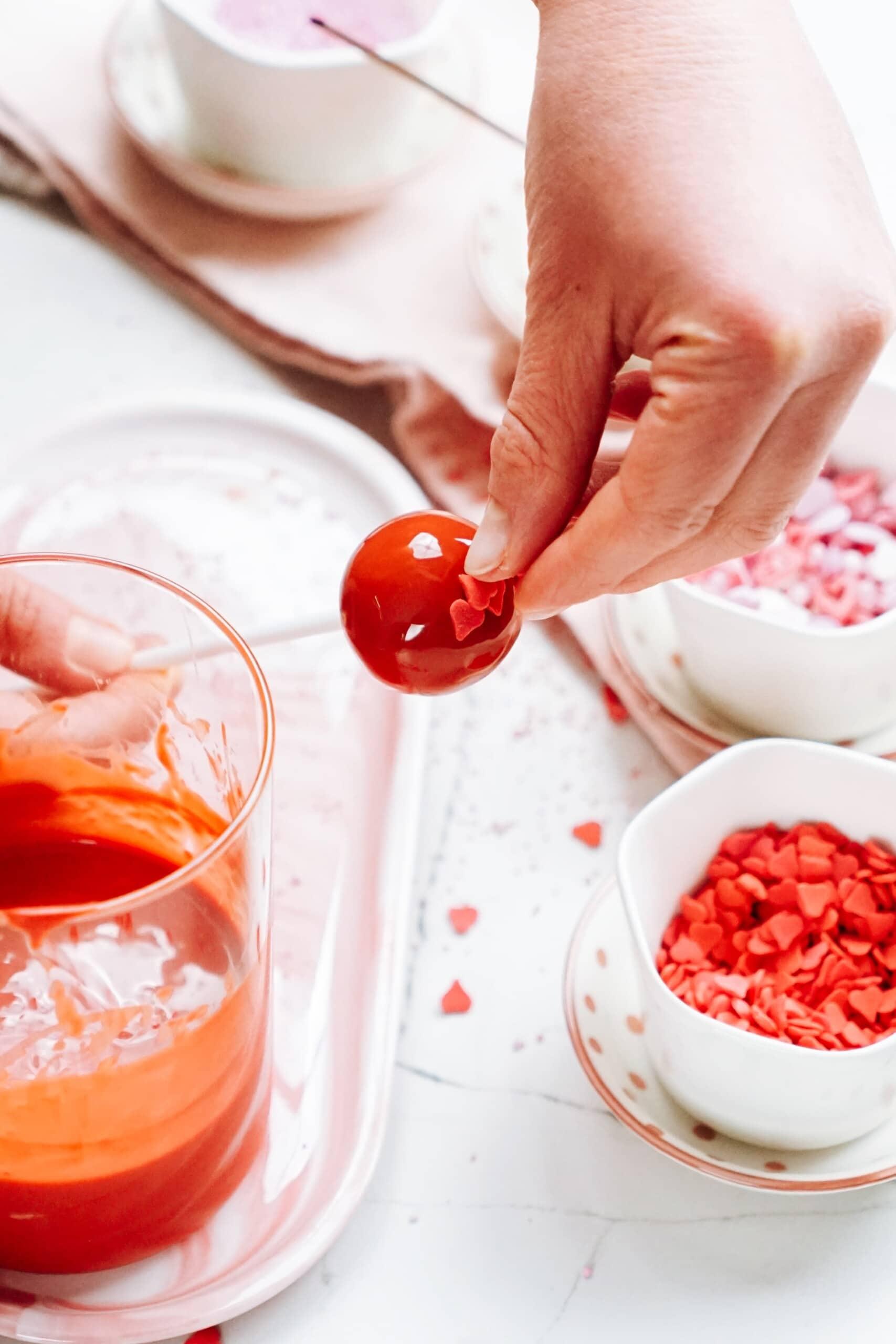 womans hand holding a cake pop while adding jimmies to the top