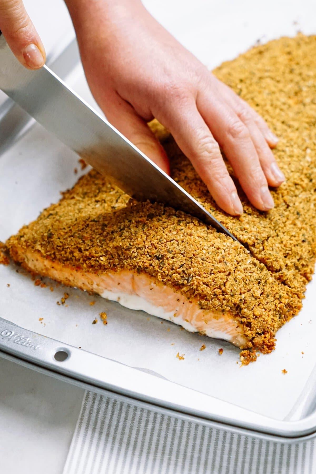 womans hand cutting salmon into portions with a knife