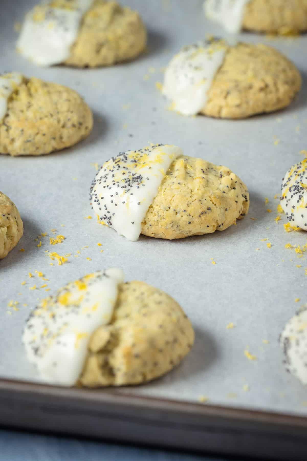 Glazed vegan lemon poppy seed cookies on a baking tray lined with parchment paper.