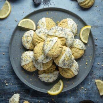 Vegan Lemon Poppy Seed cookies stacked on a grey plate served with sprinkles of poppy seeds and lemon wedges.