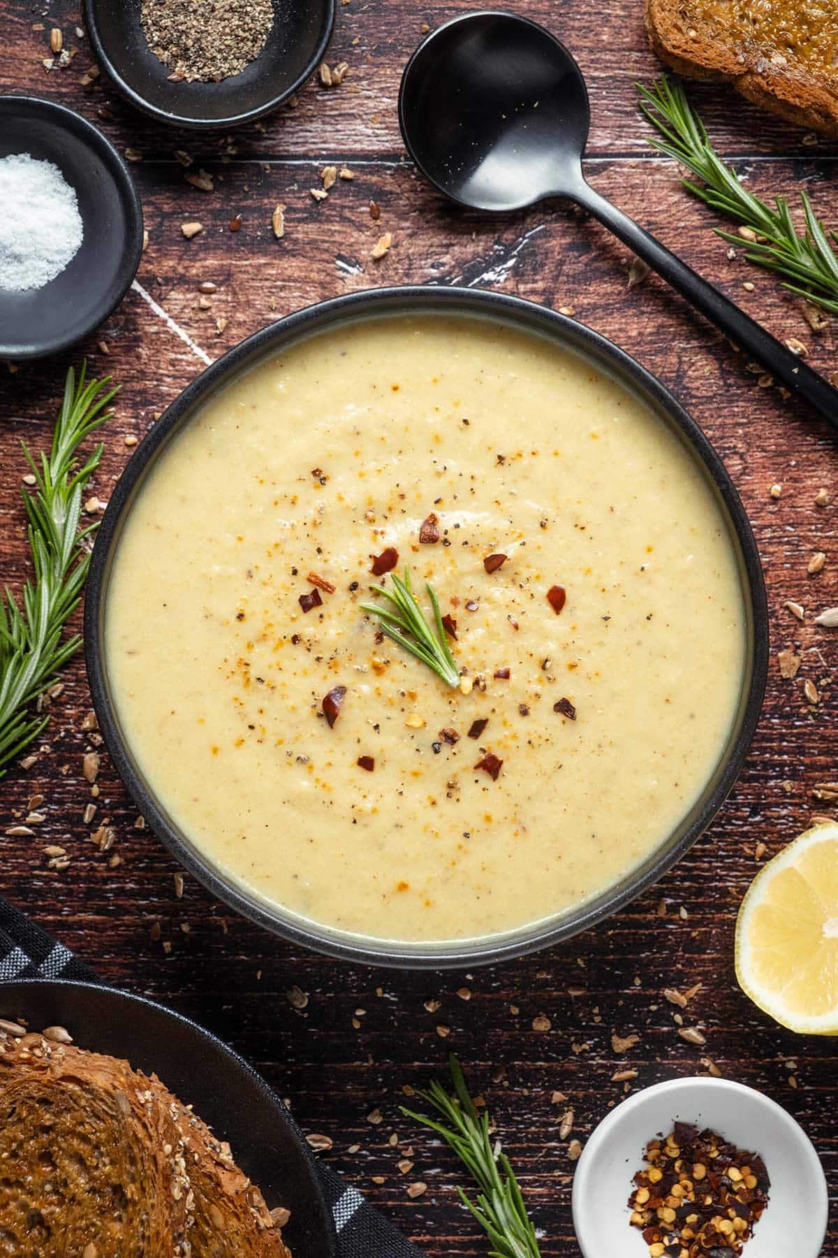 Vegan Roasted Cauliflower Soup served in a black bowl with a side serving of fresh bread.