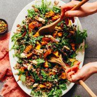 Using wood serving spoons to pick up a serving of roasted squash salad